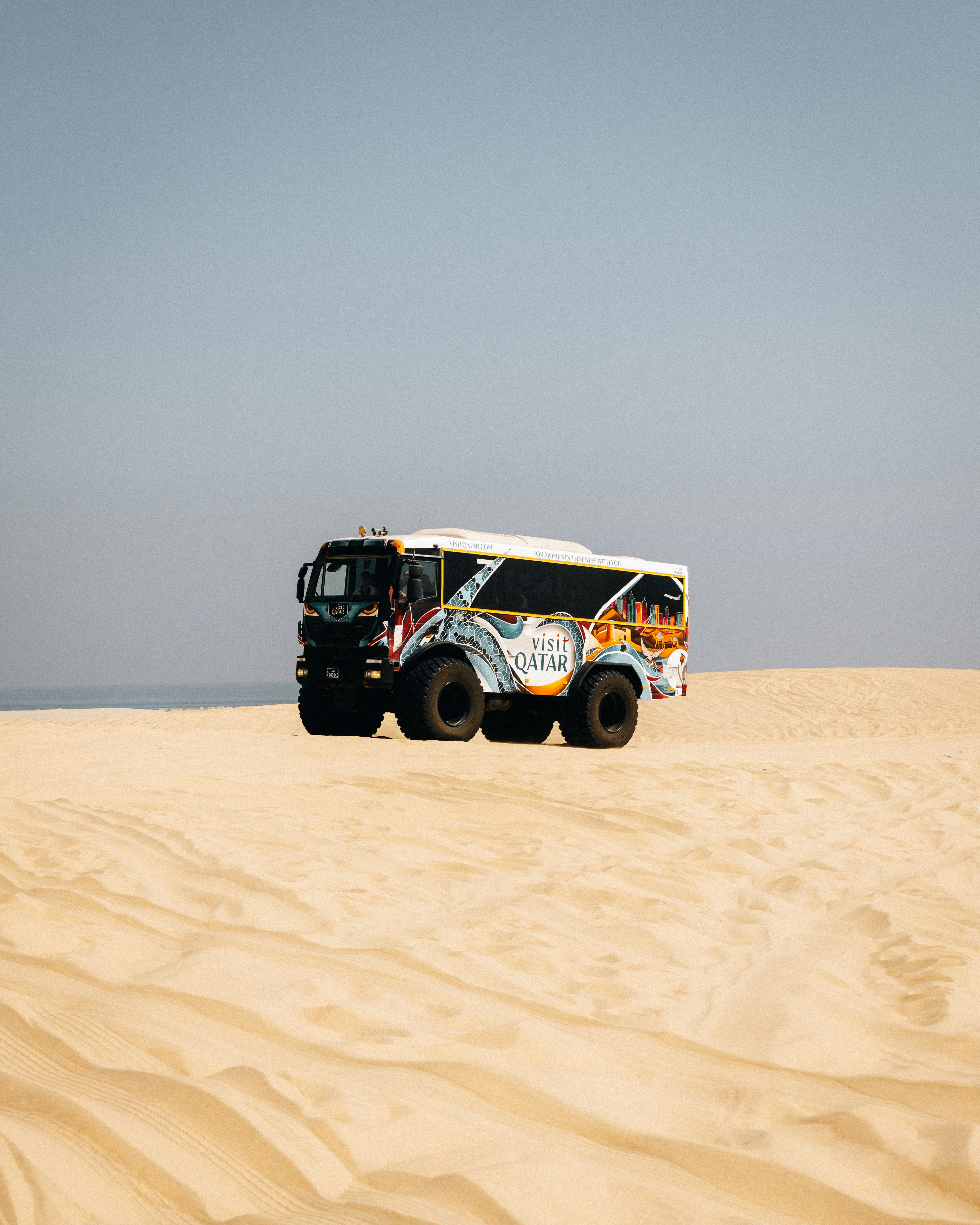 A unique vehicle drives across a sandy desert landscape.