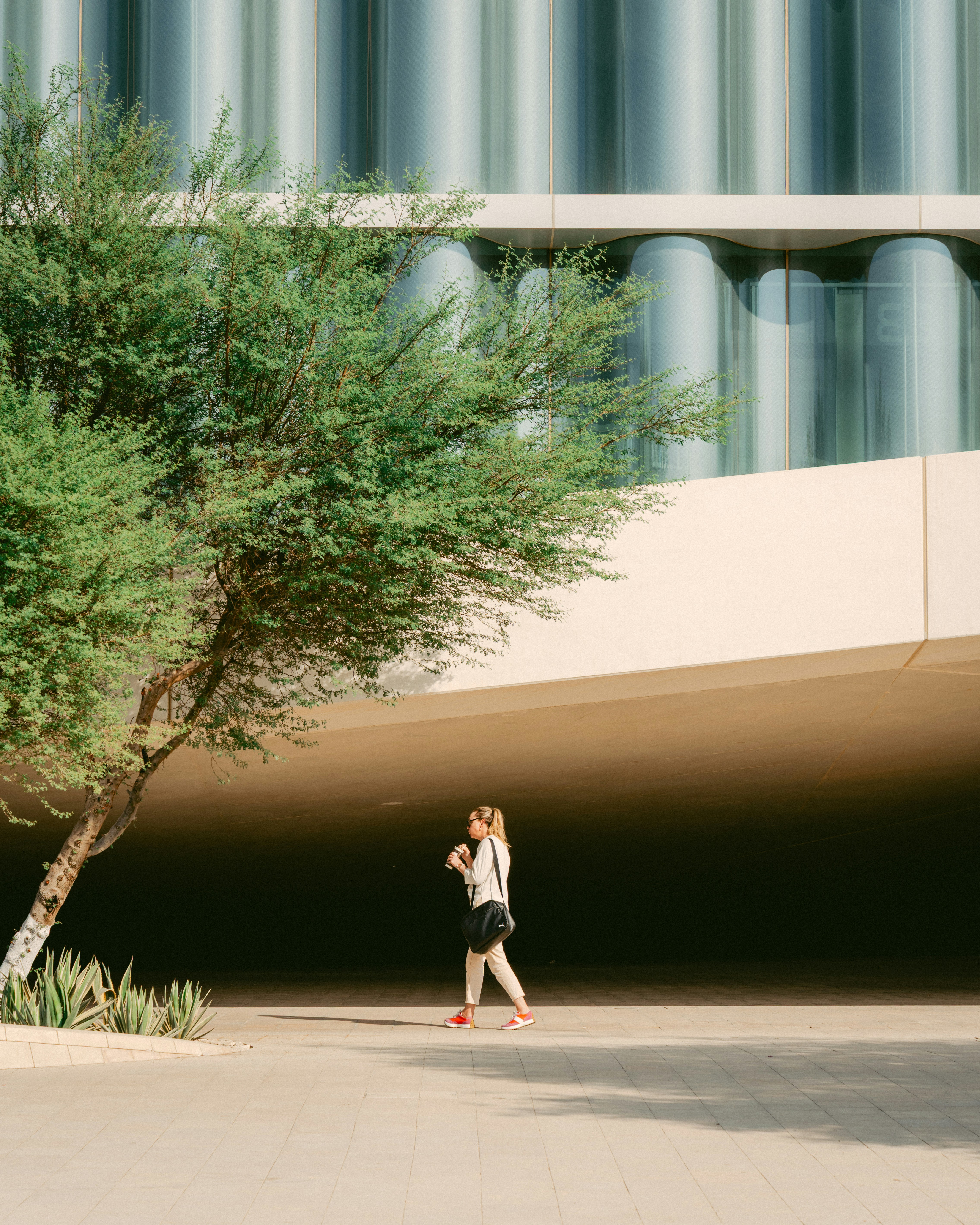 Woman walking past a modern building with a tree.