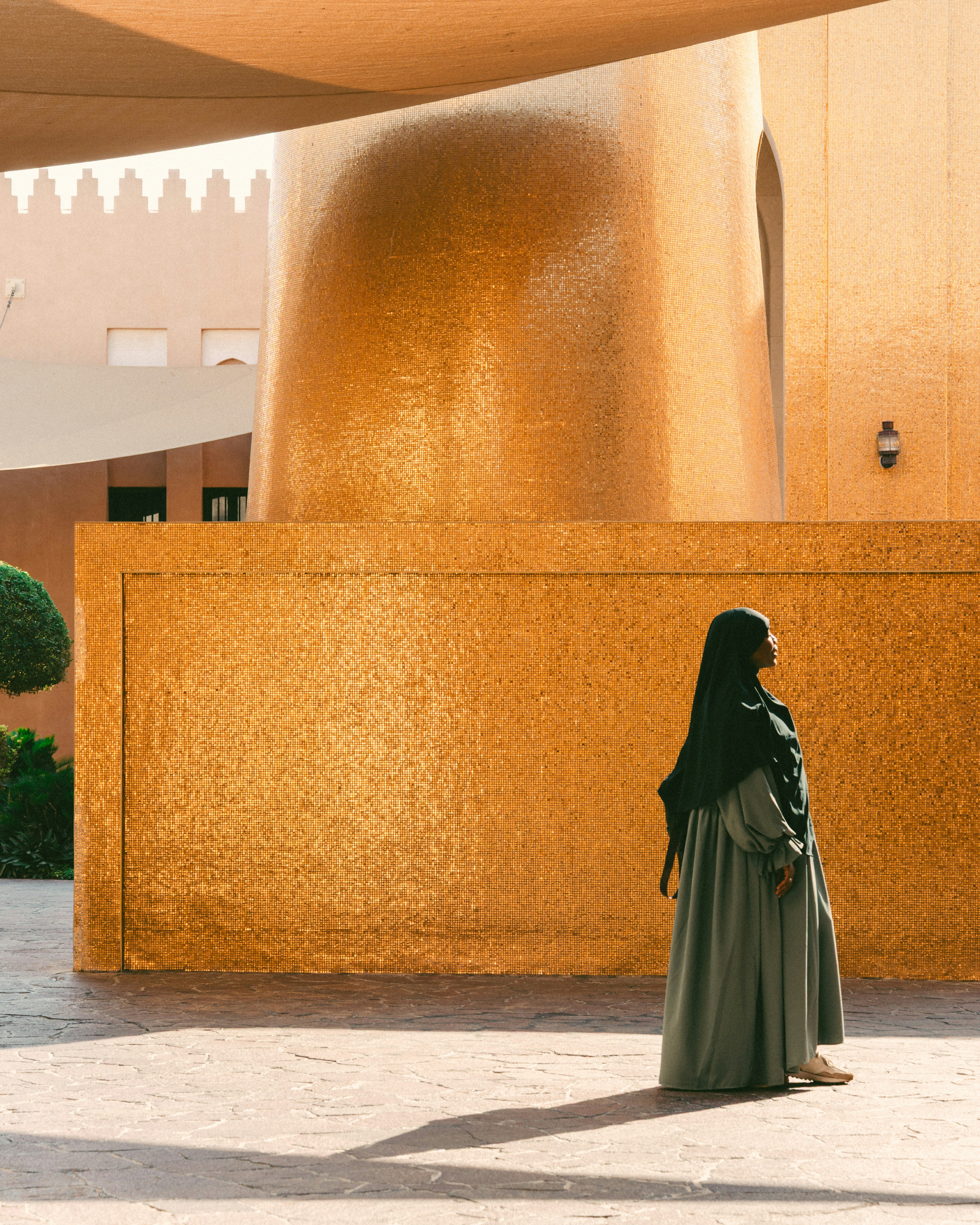 Woman in hijab stands near a golden building.