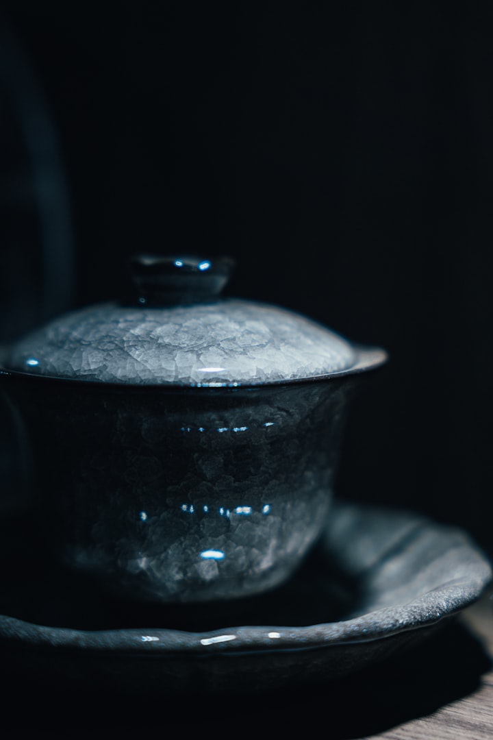A dark, cracked ceramic gaiwan tea bowl with lid and saucer, evoking the ceremonial gongfu brewing setup