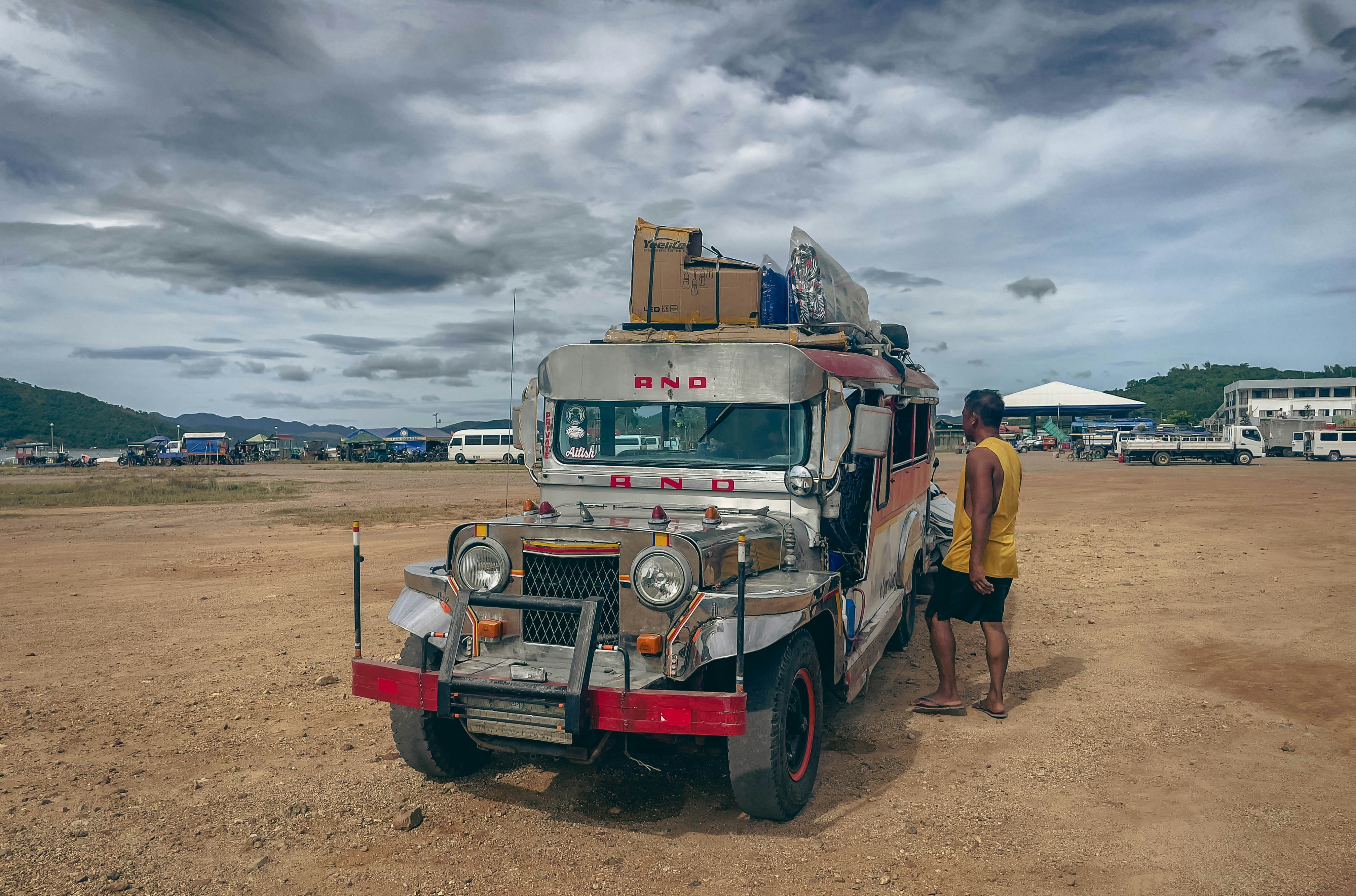 Man standing beside a loaded jeepney under cloudy sky