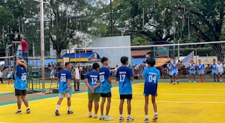 Young boys playing volleyball on a bright yellow court.