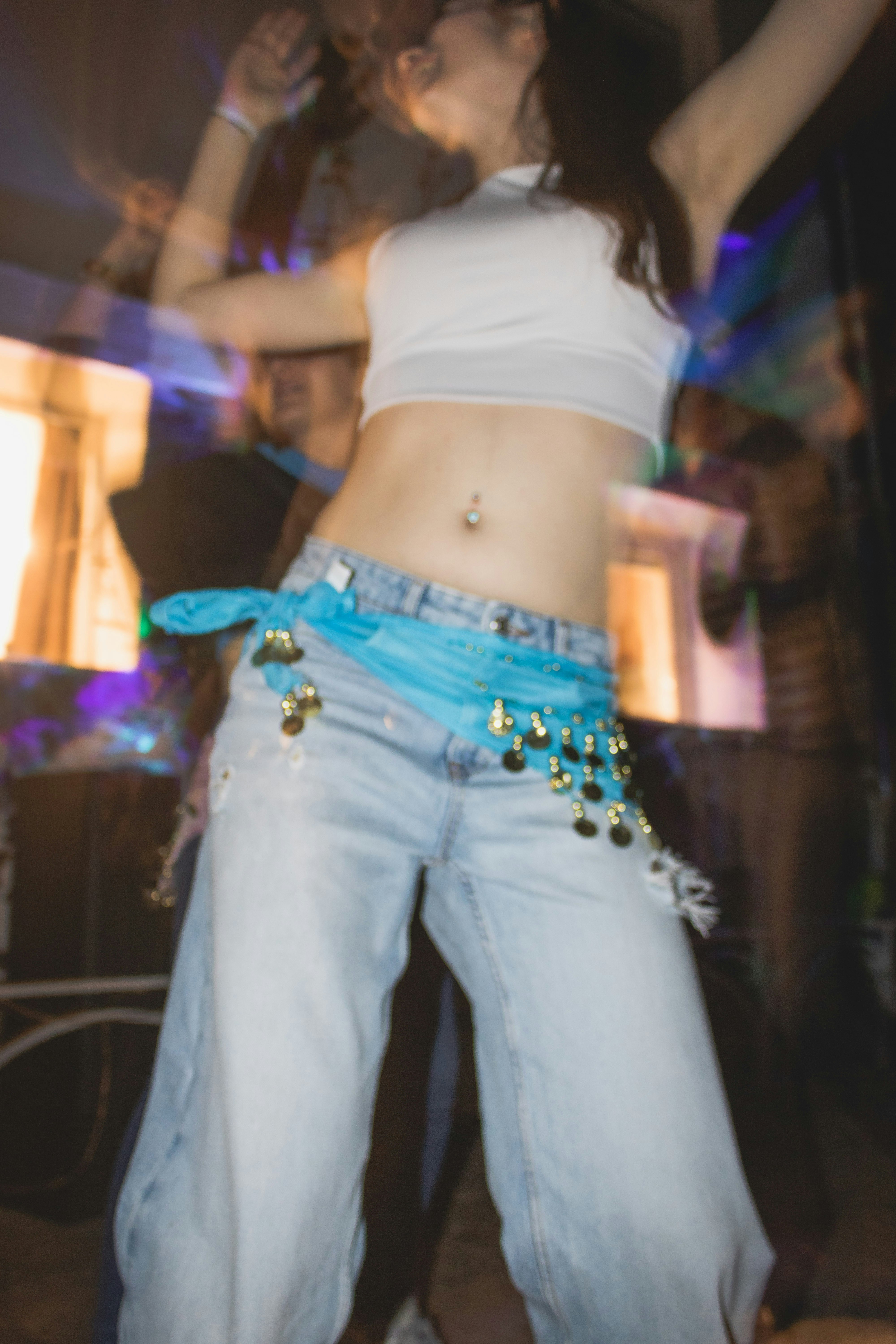 ジーンズと青いサッシュを身に着け、腕を上げて踊る女性。