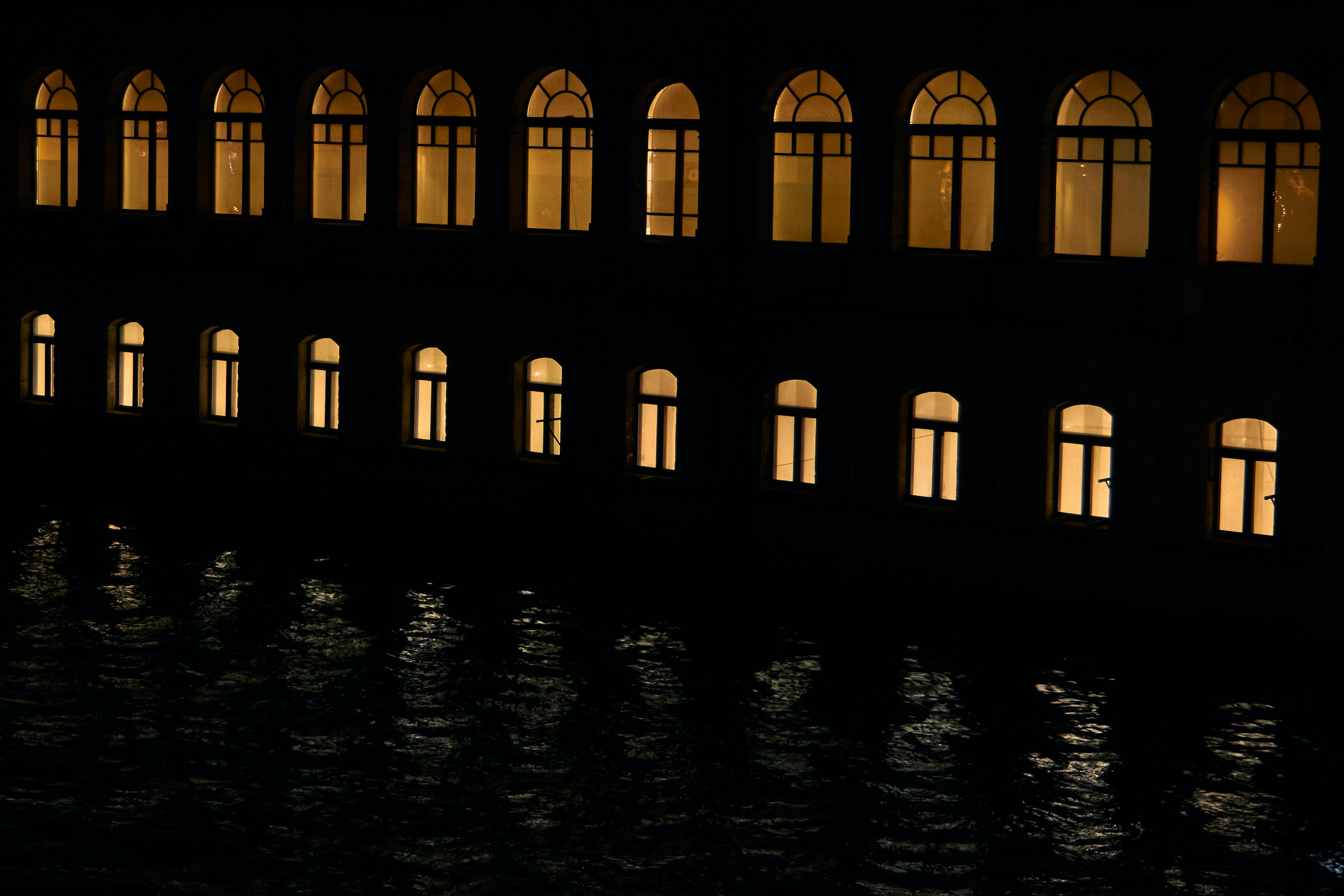 Building windows illuminated at night reflecting in water.