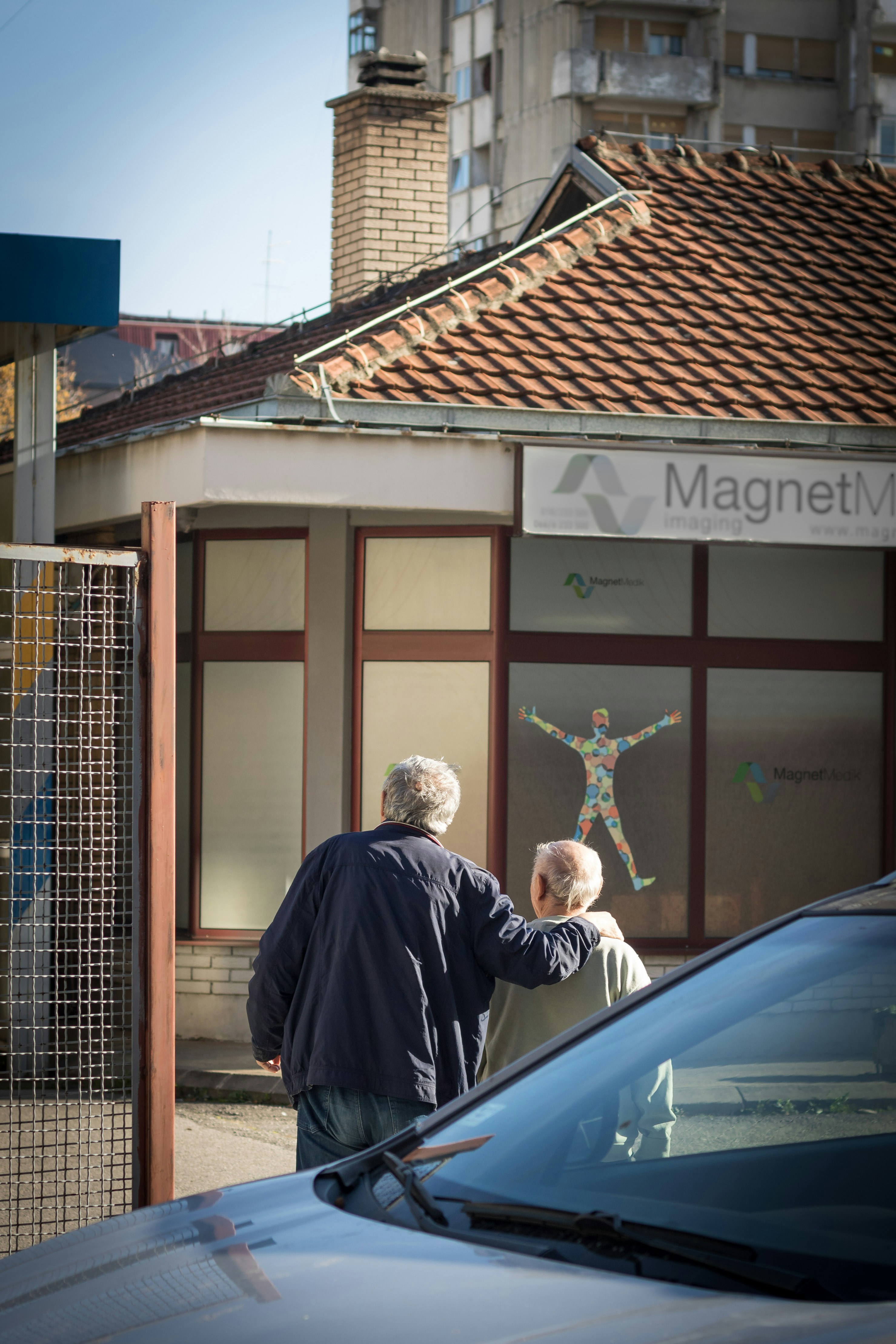 Two elderly men walk past a building with artwork.