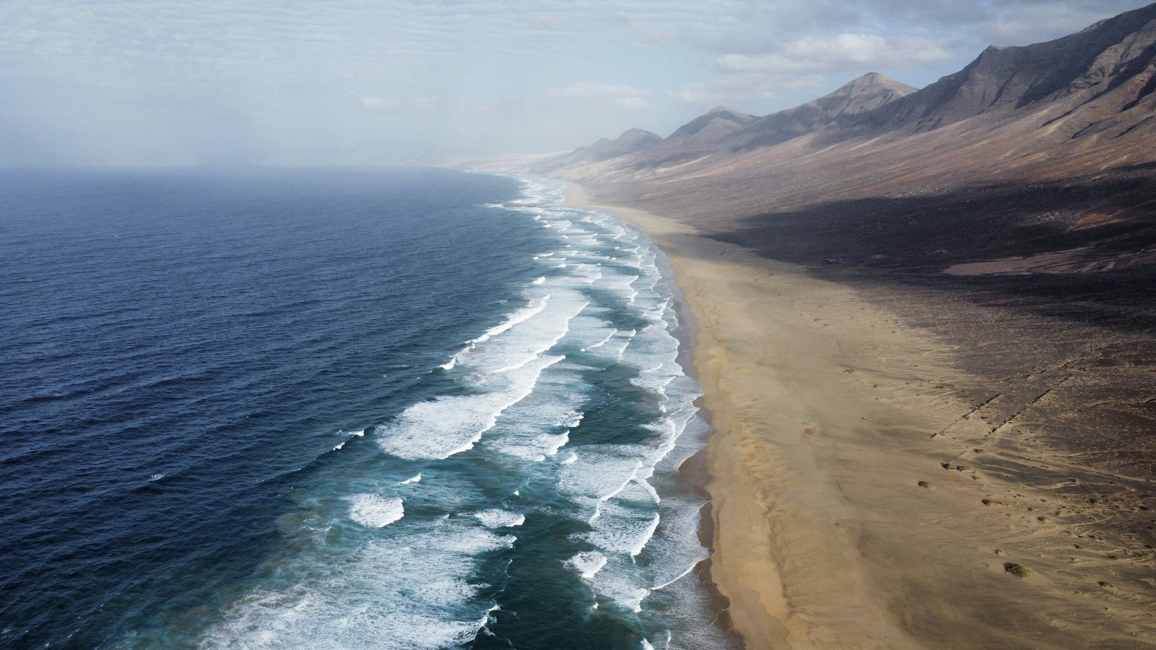 Ocean waves crash on a sandy beach with mountains.