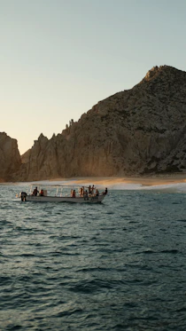 Tour boat sailing near rocky coastline at sunset