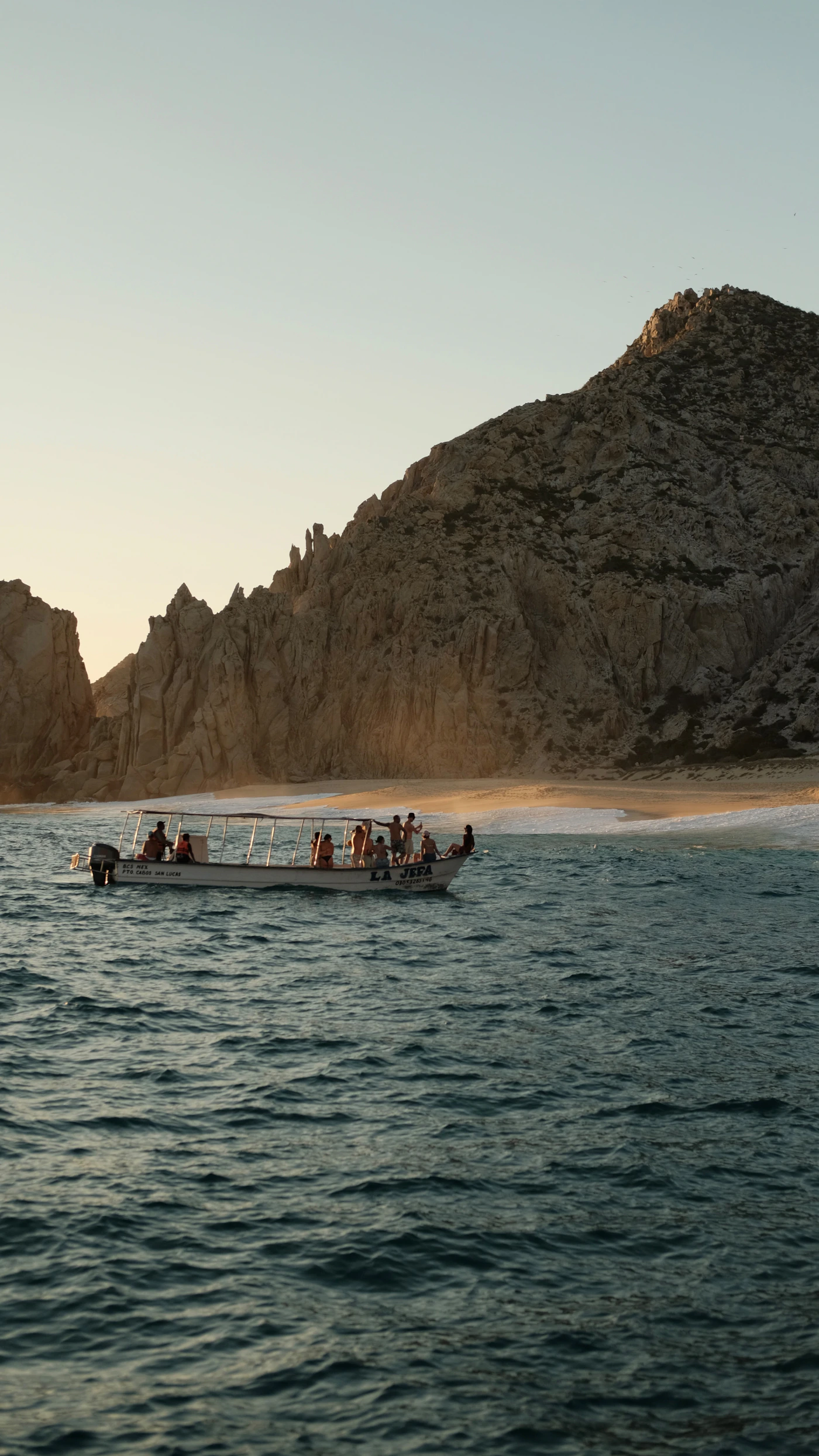 Tour boat sailing near the rocky coastline of Los Cabos Baja California Mexico at sunset showing the dramatic coastal geology of the southern Baja Peninsula