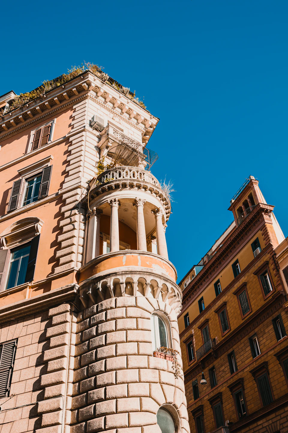 Tall, ornate building with curved facade and balcony on second floor in orange hues