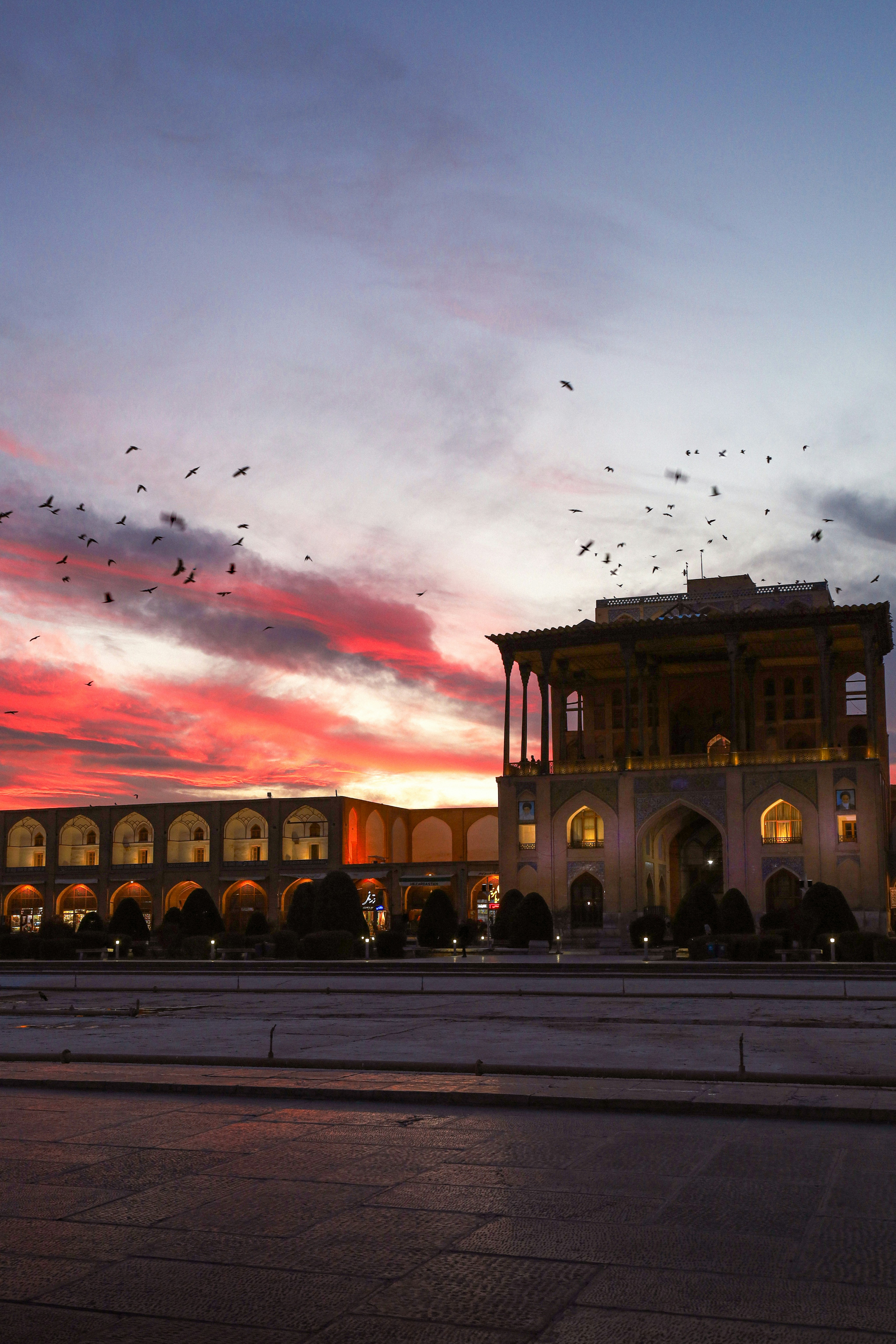 Birds fly over a palace at sunset.