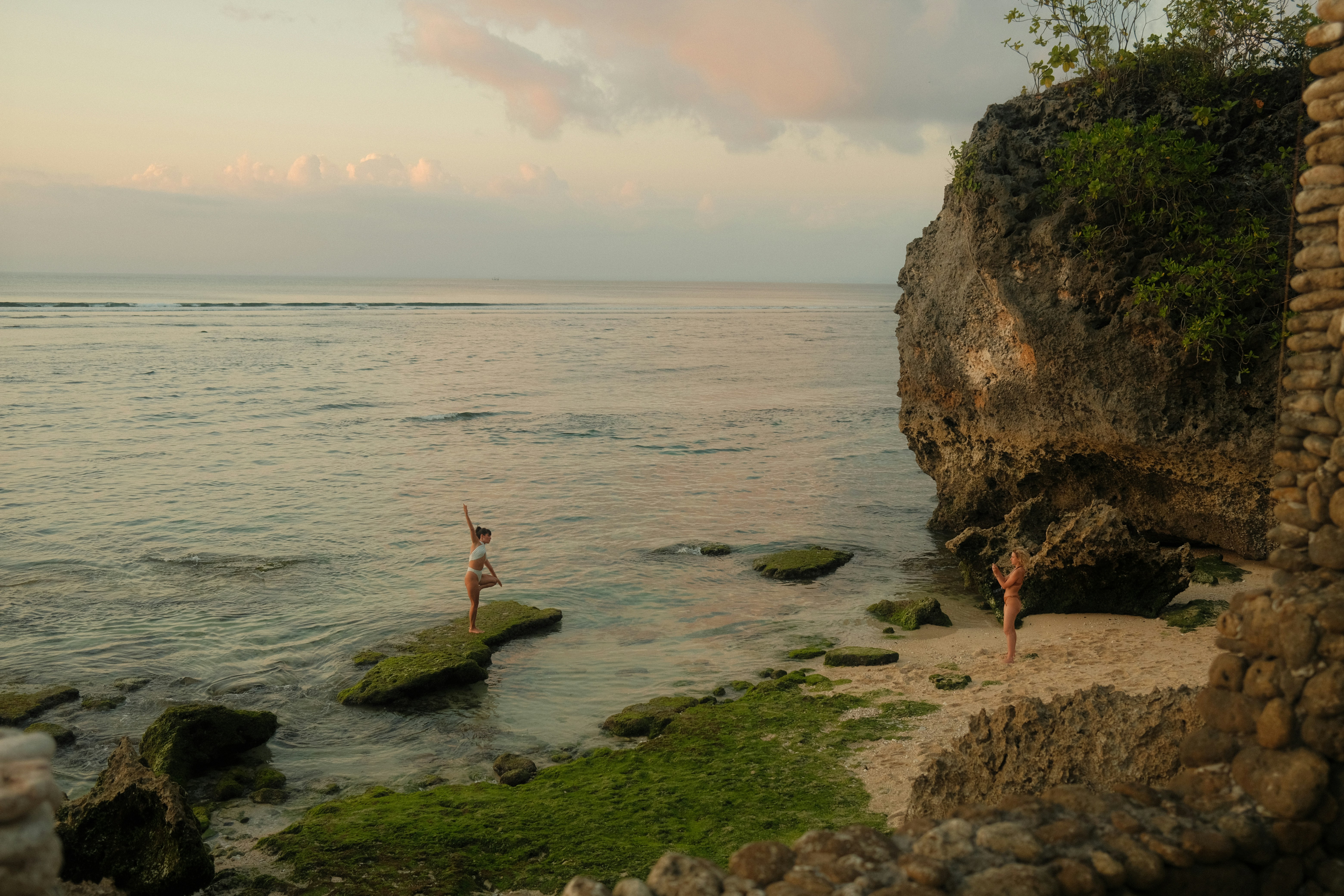 Two people stand on rocks by the ocean.