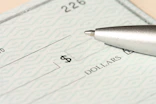 A pen rests on a check near the dollars line.
