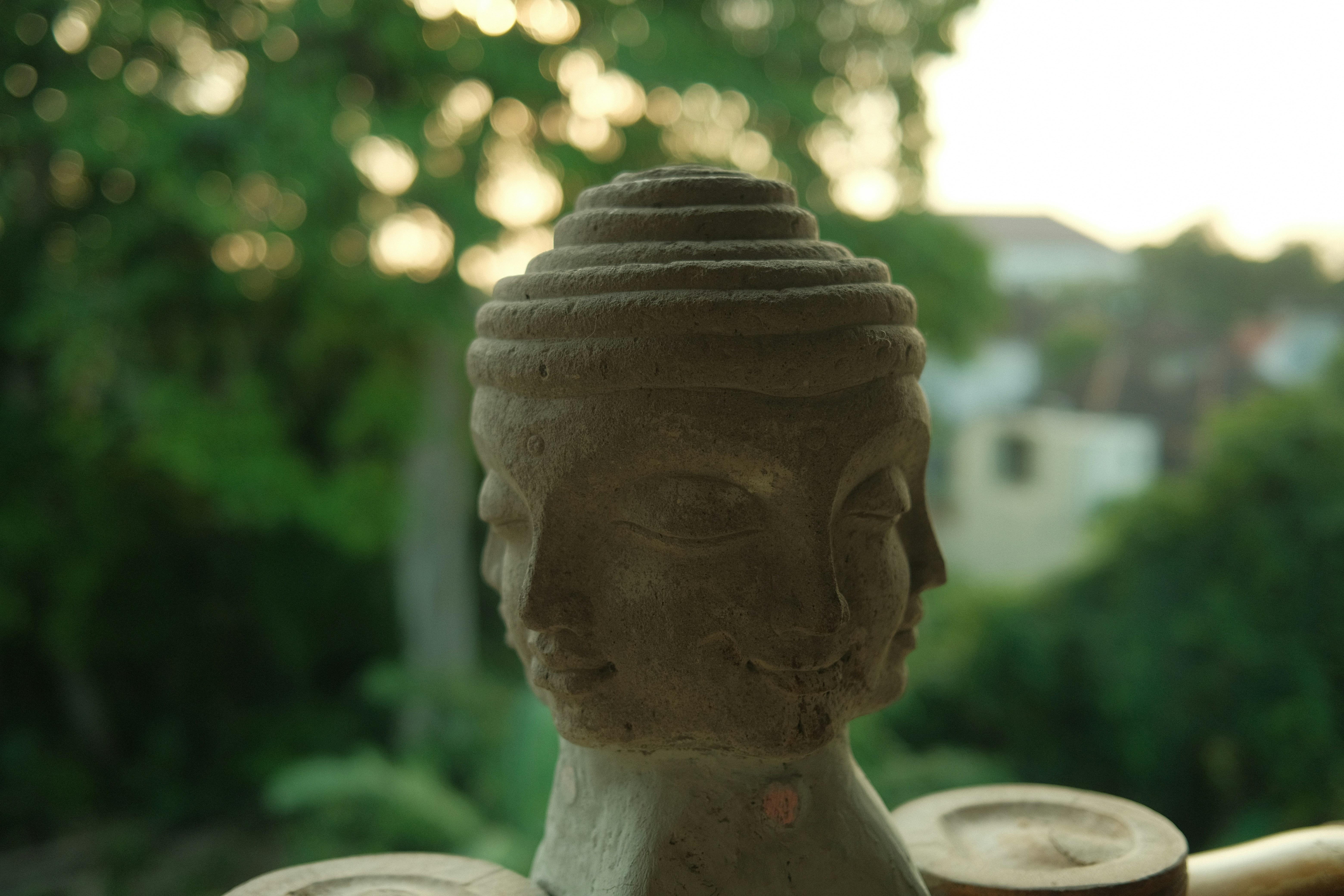 A stone buddha head statue with blurred trees
