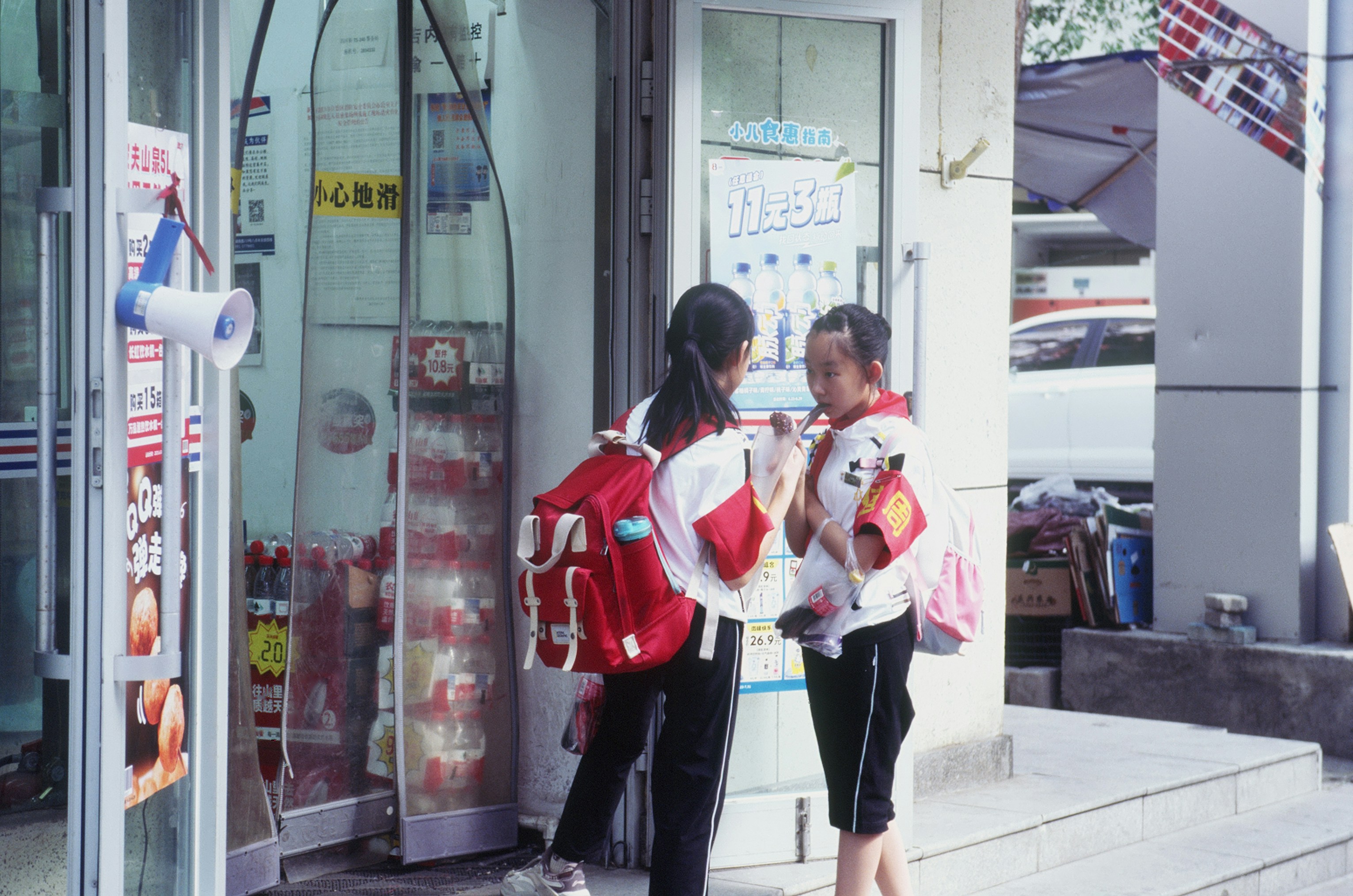 Two girls with backpacks talking outside a store.