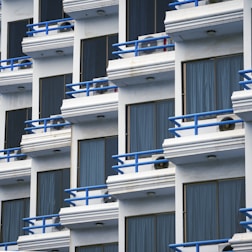 Rows of white balconies with blue railings on building.