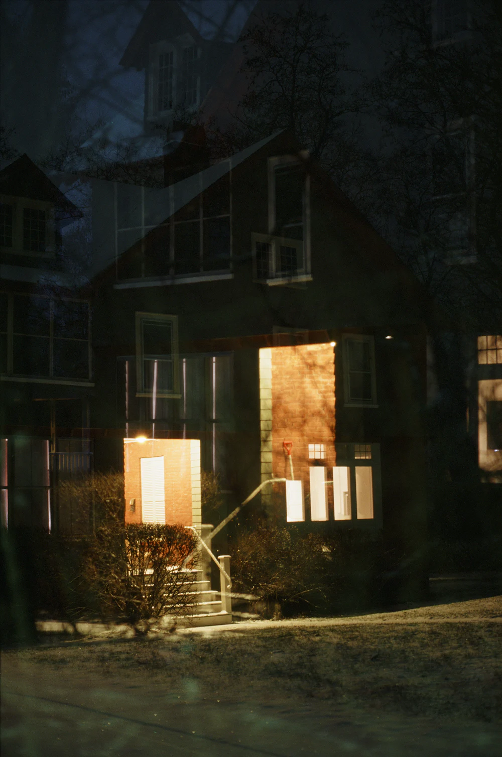 A dark clapboard house at night with warm light in its windows and open door.