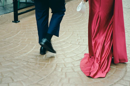 Couple walking in elegant attire on patterned floor.