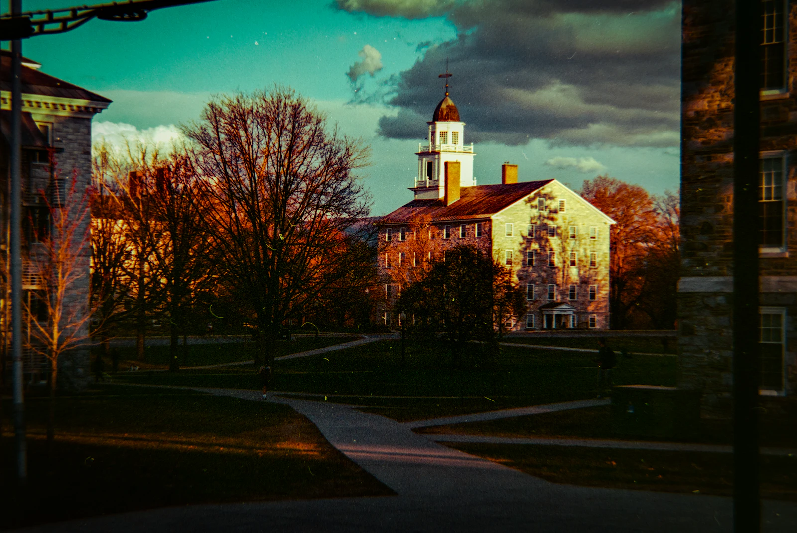 Historic college buildings behind a lawn at dusk.