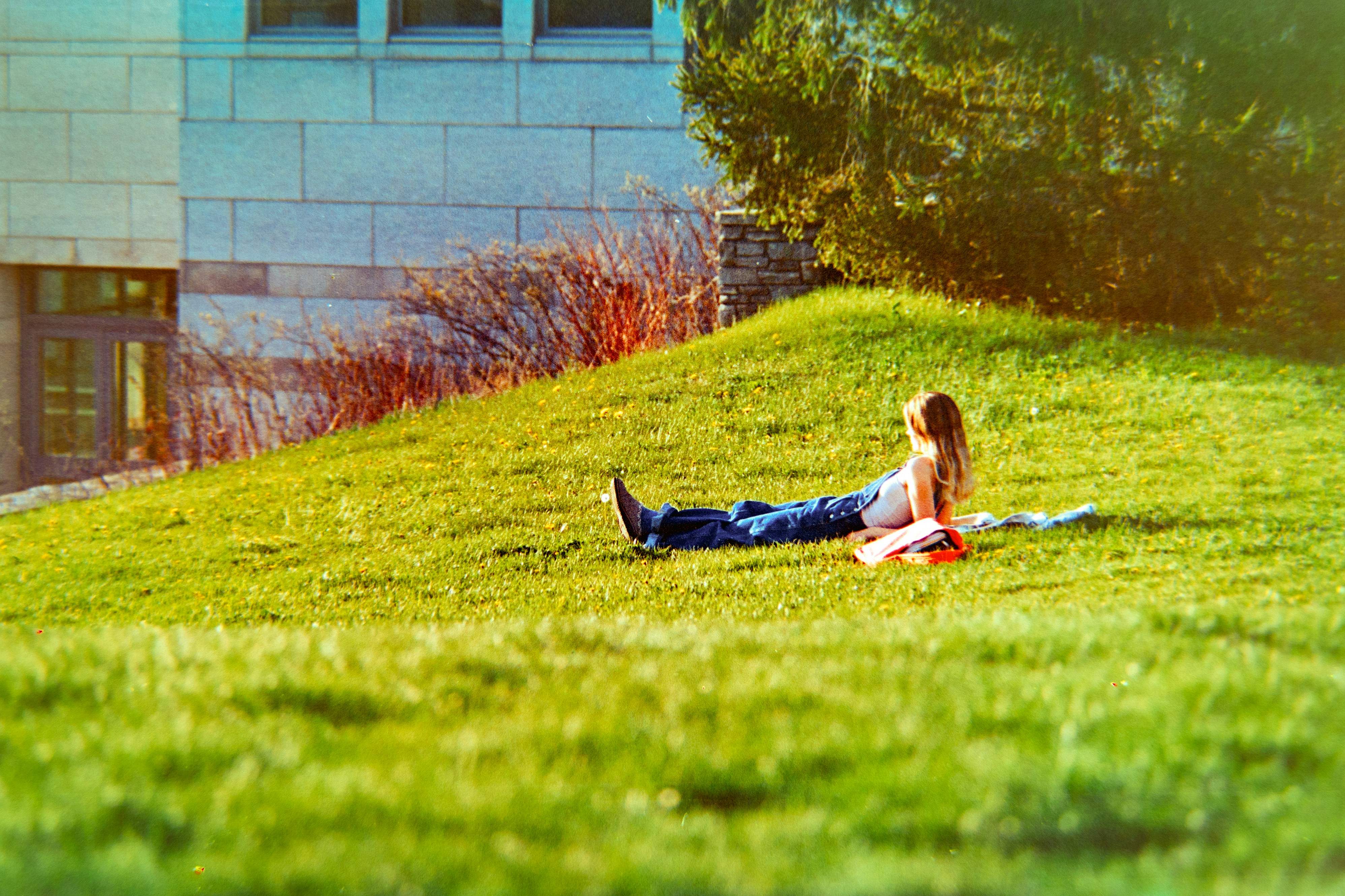 Eine Person entspannt sich auf einem grasbewachsenen Hügel in der Nähe eines Gebäudes.