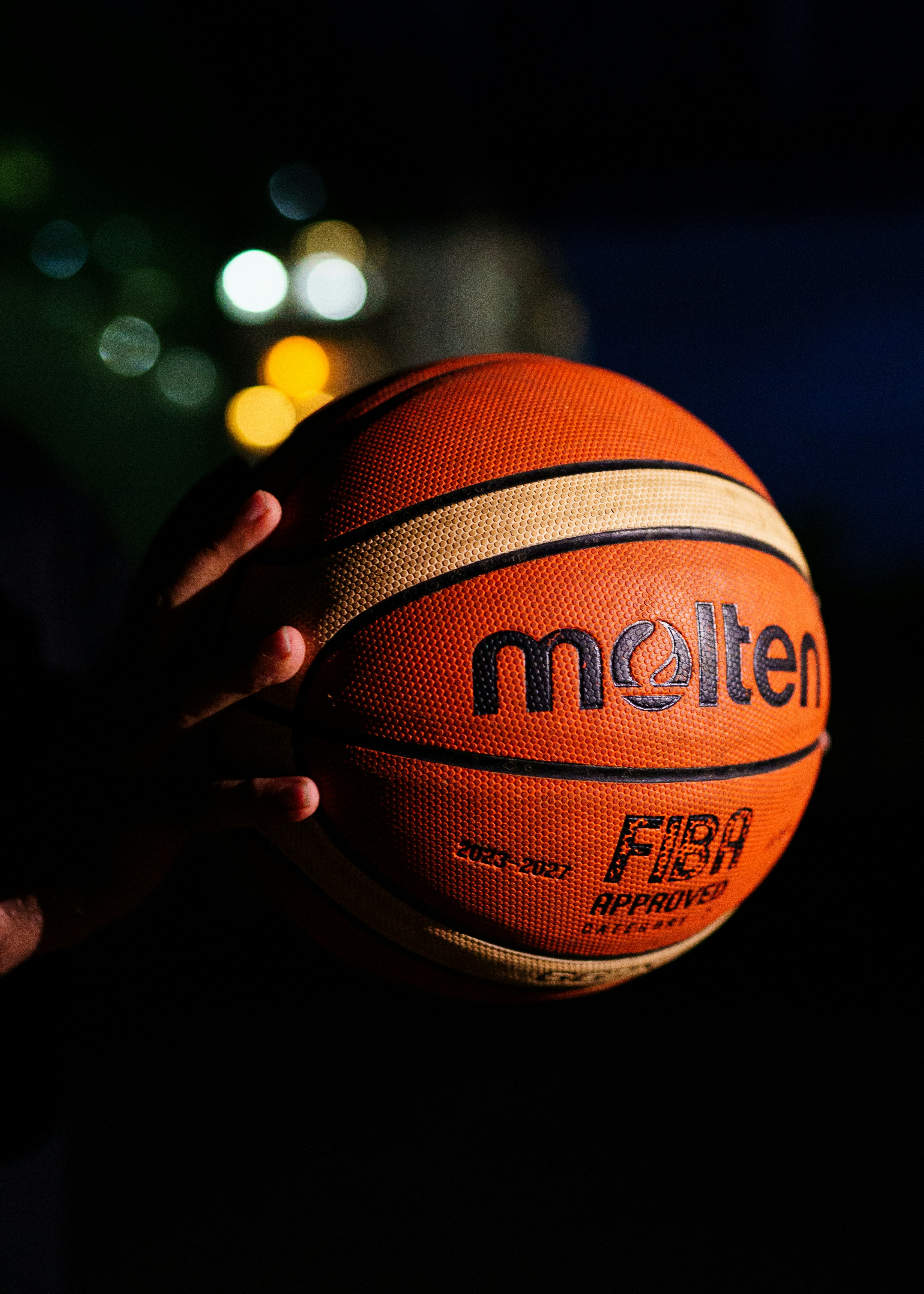 Hand holding a molten basketball at night.