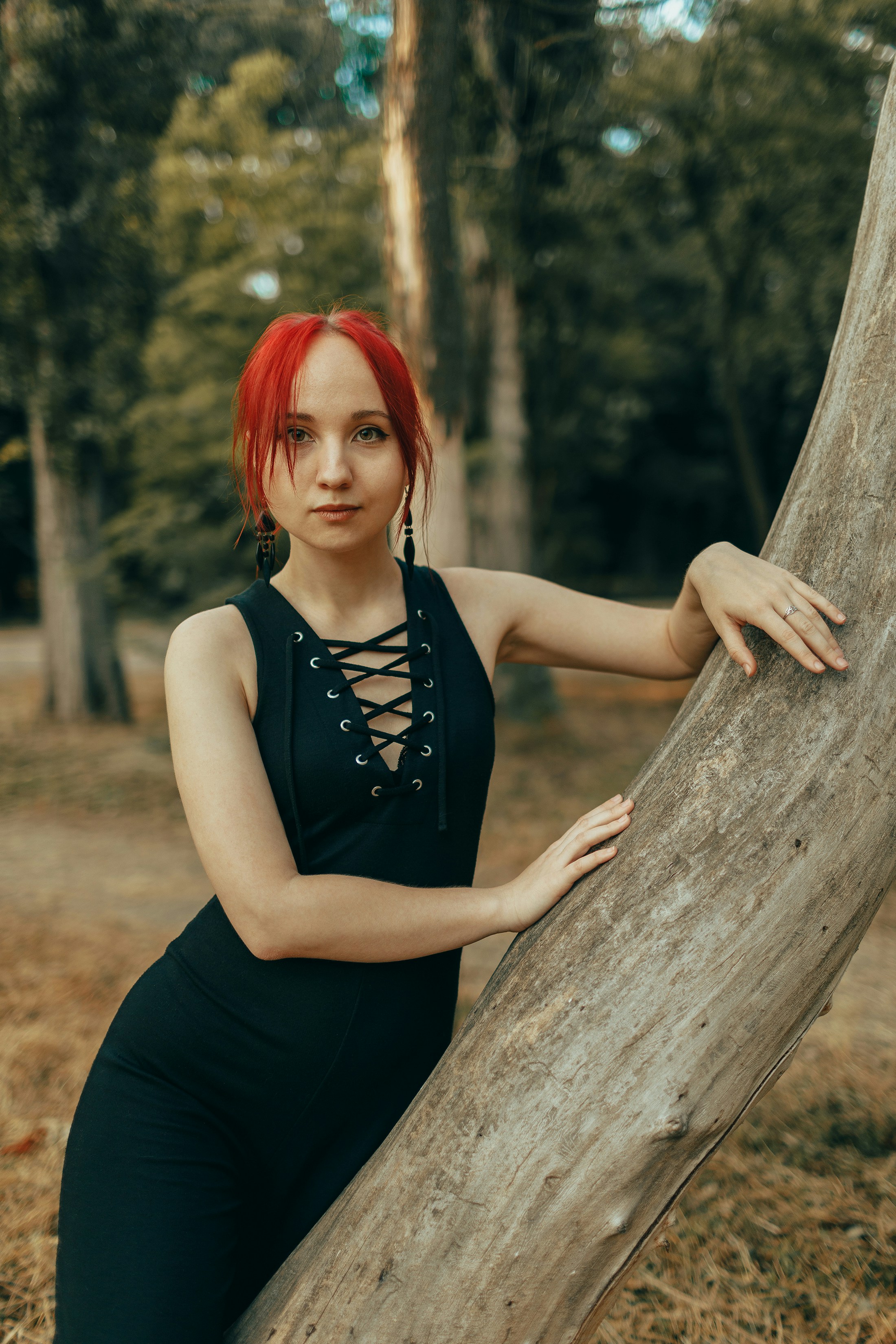 Donna con capelli rossi in abito nero appoggiata all'albero.
