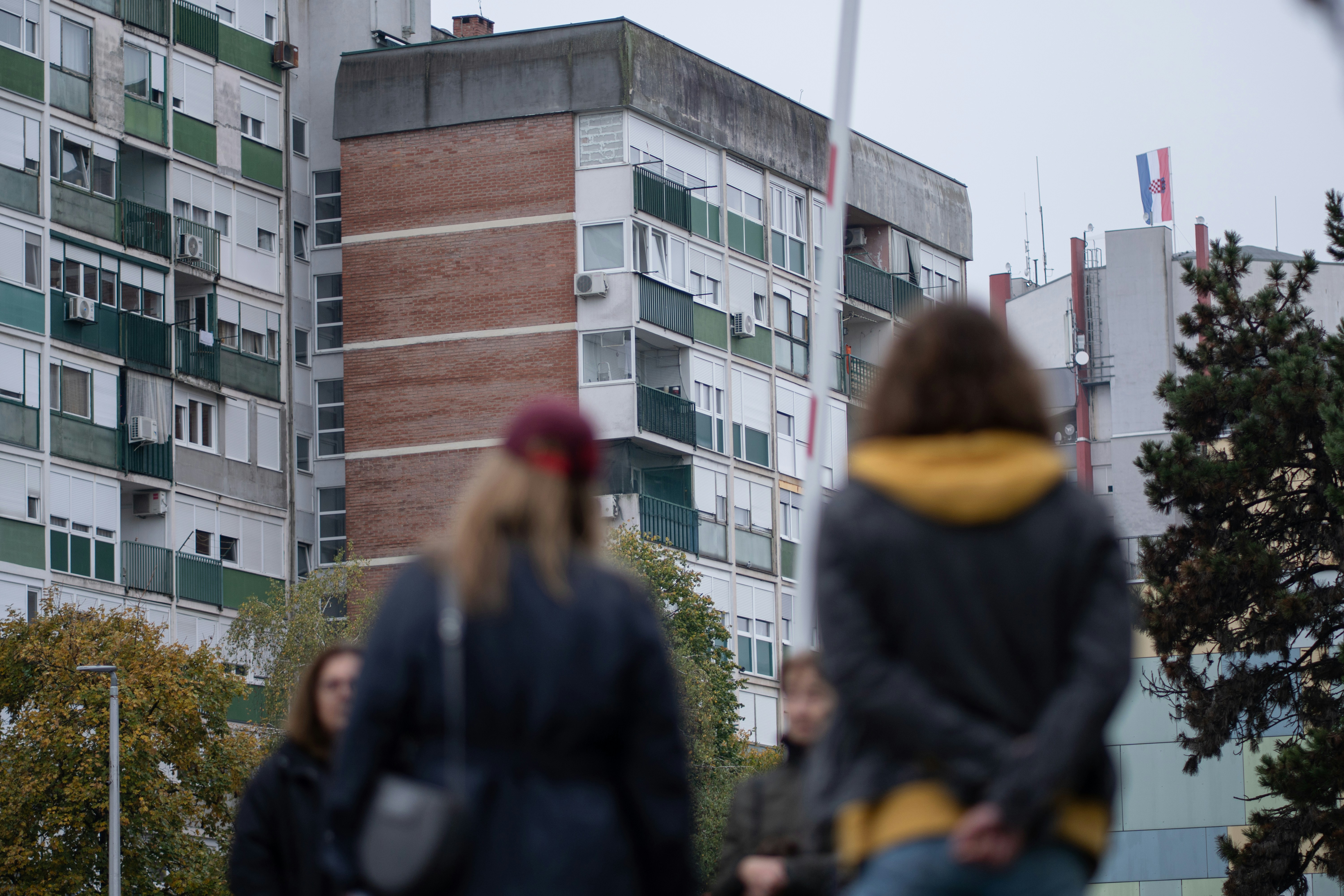 People walking past apartment buildings on a cloudy day.