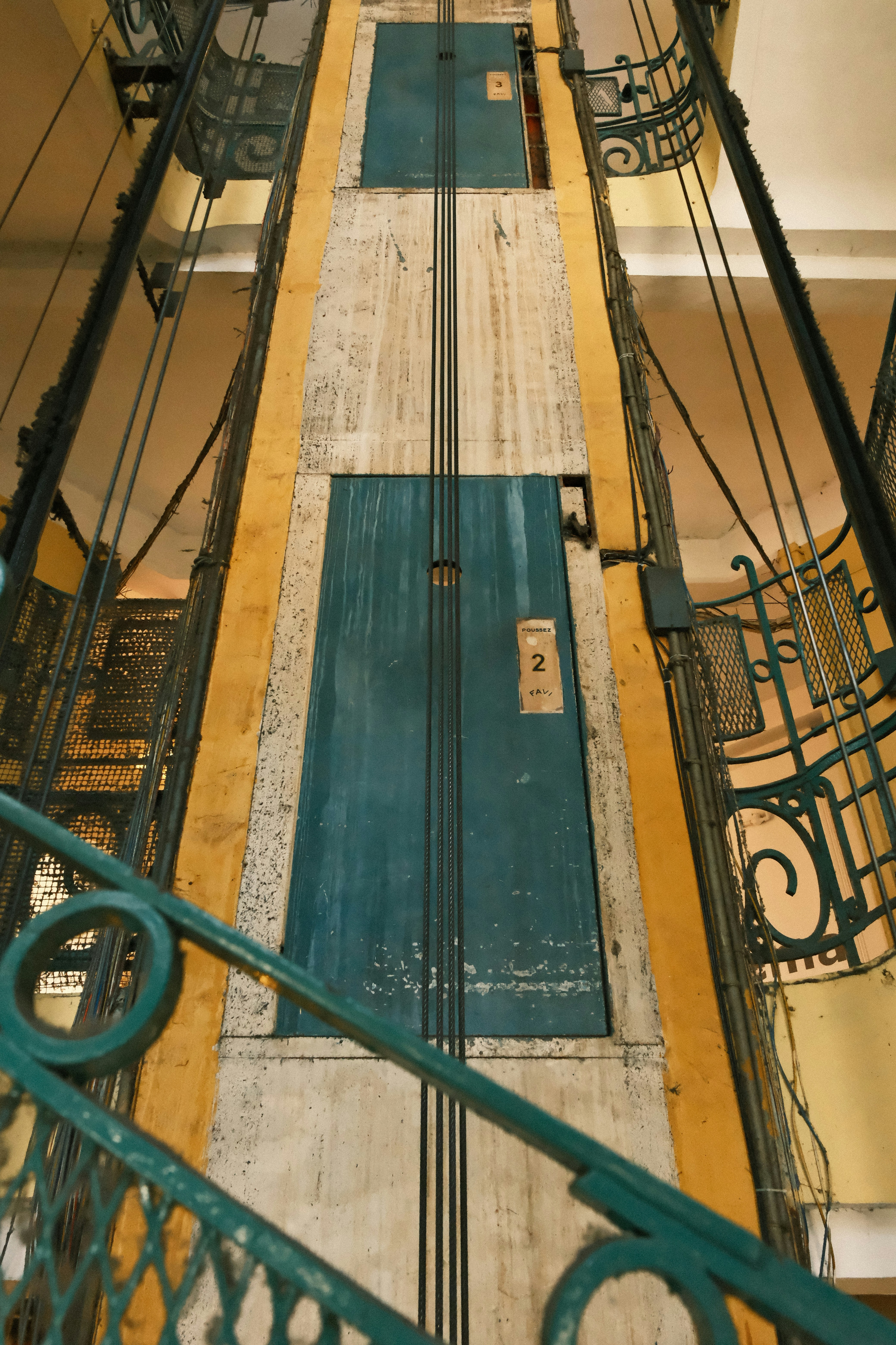 Vintage elevator shaft with teal doors and metal railings.