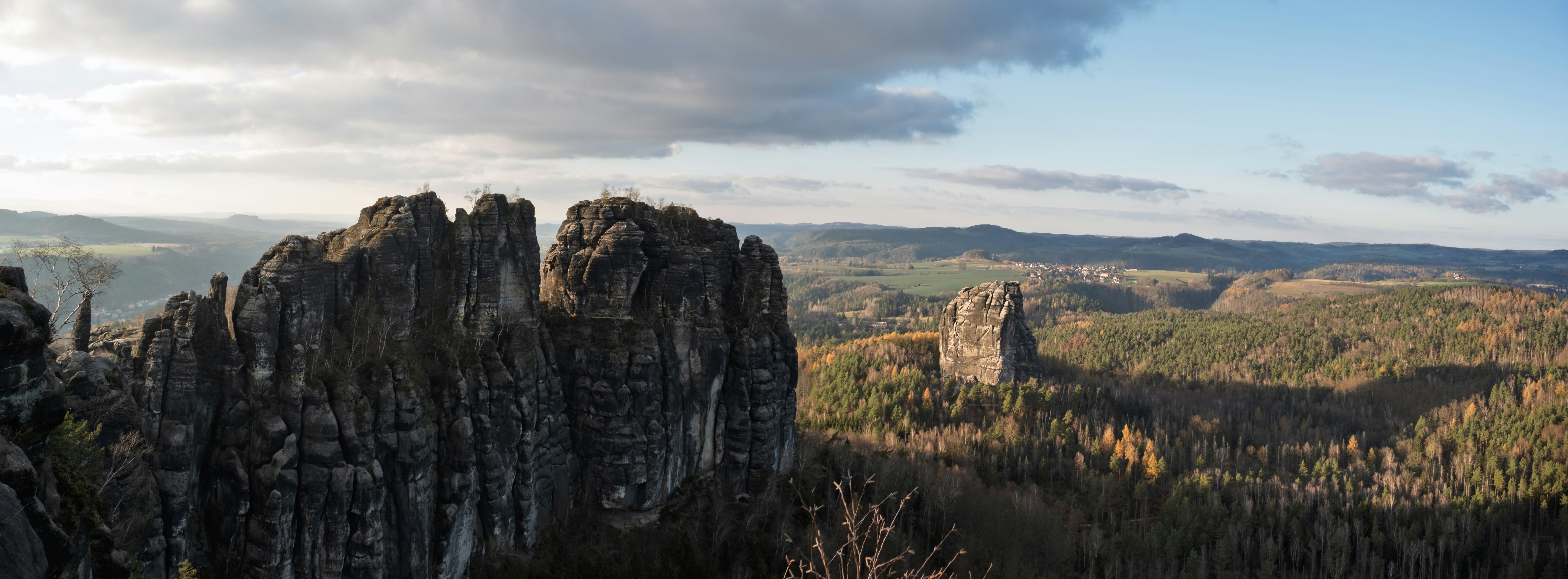 岩だらけの峰々が、曇り空の下、森林に覆われた谷を見下ろしています。