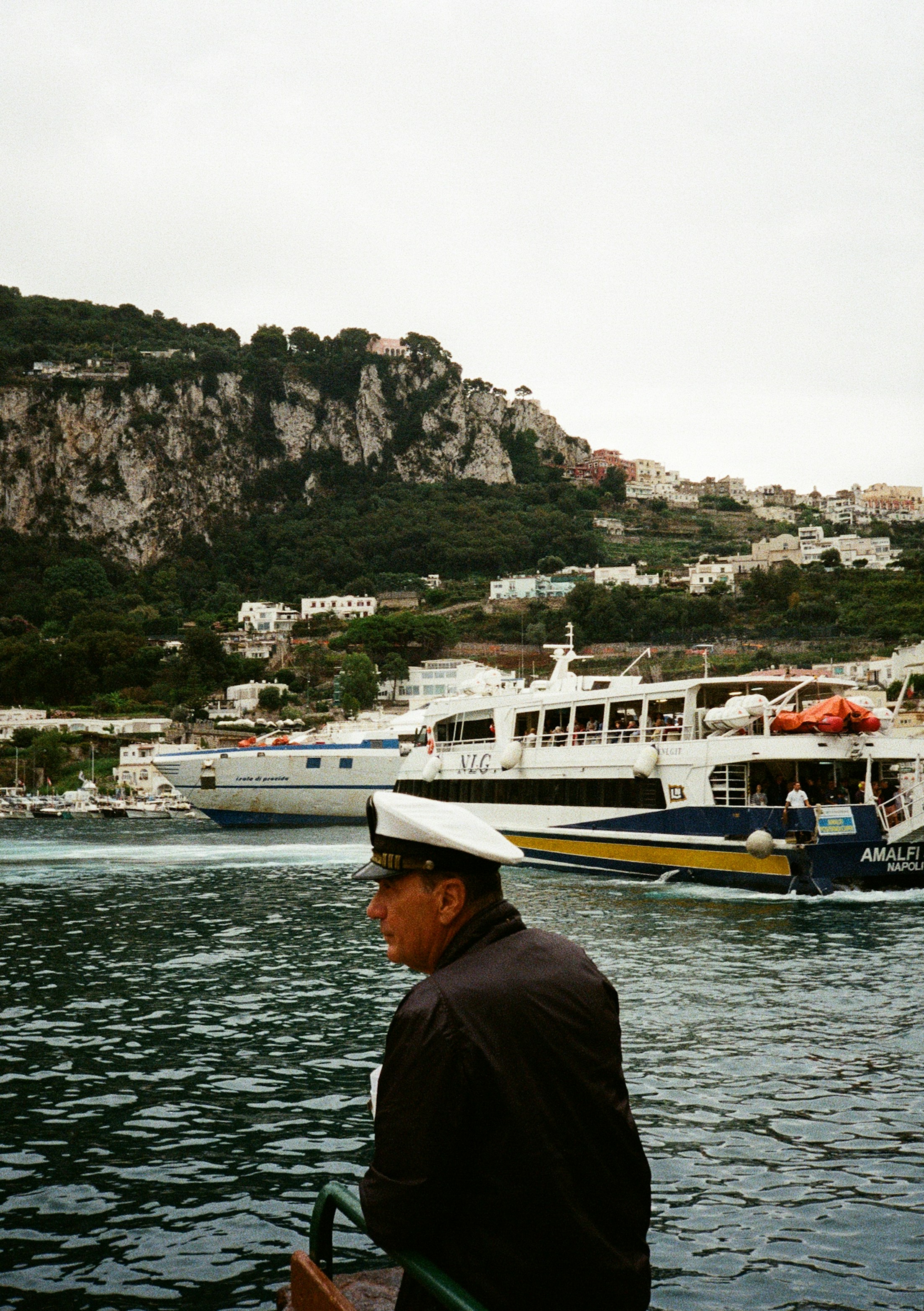 Man in uniform on boat with ferries and island.