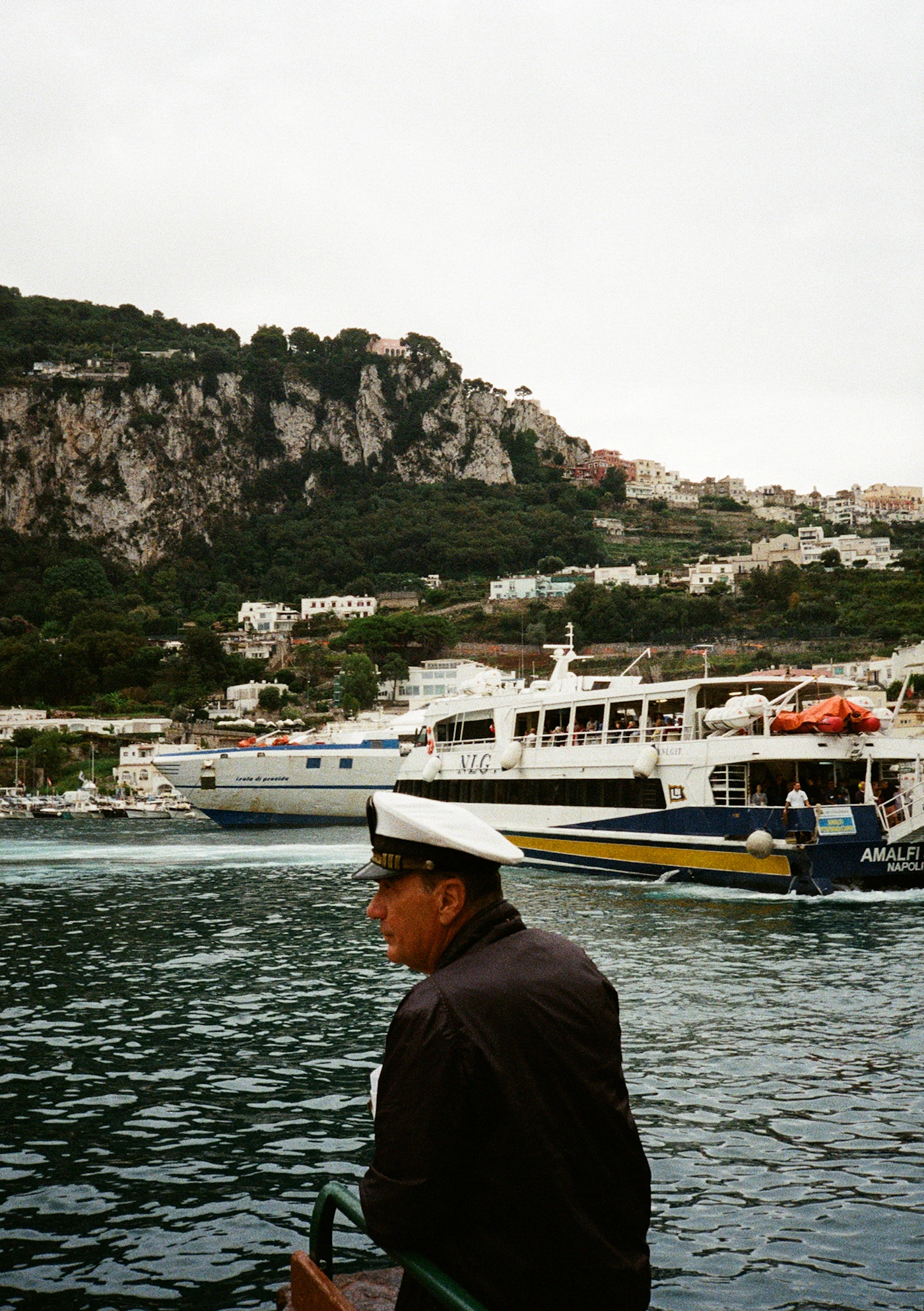 A uniformed boat captain in his peaked cap, the Amalfi coast beyond