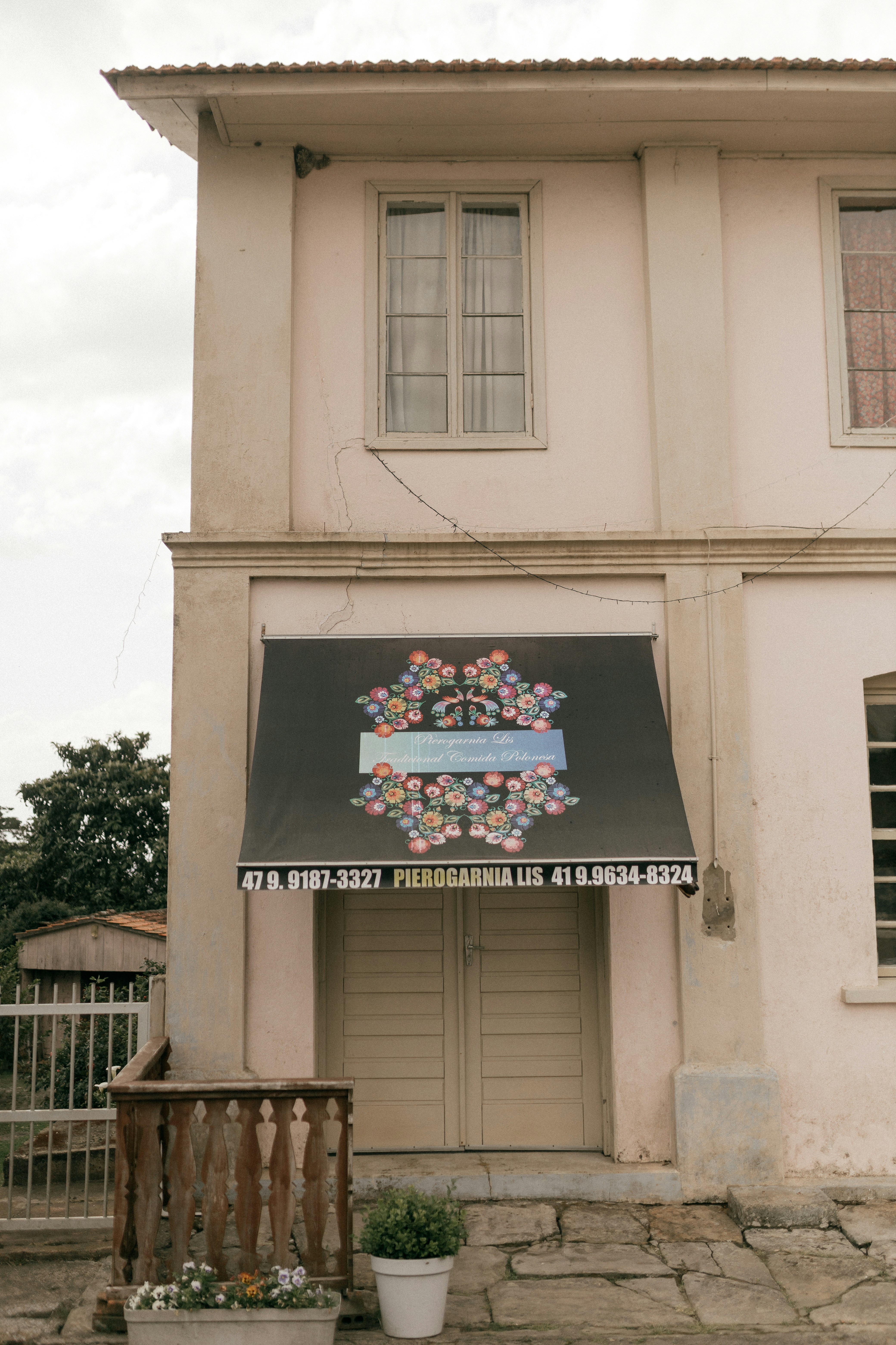 Pale pink building with a dark awning above doors.