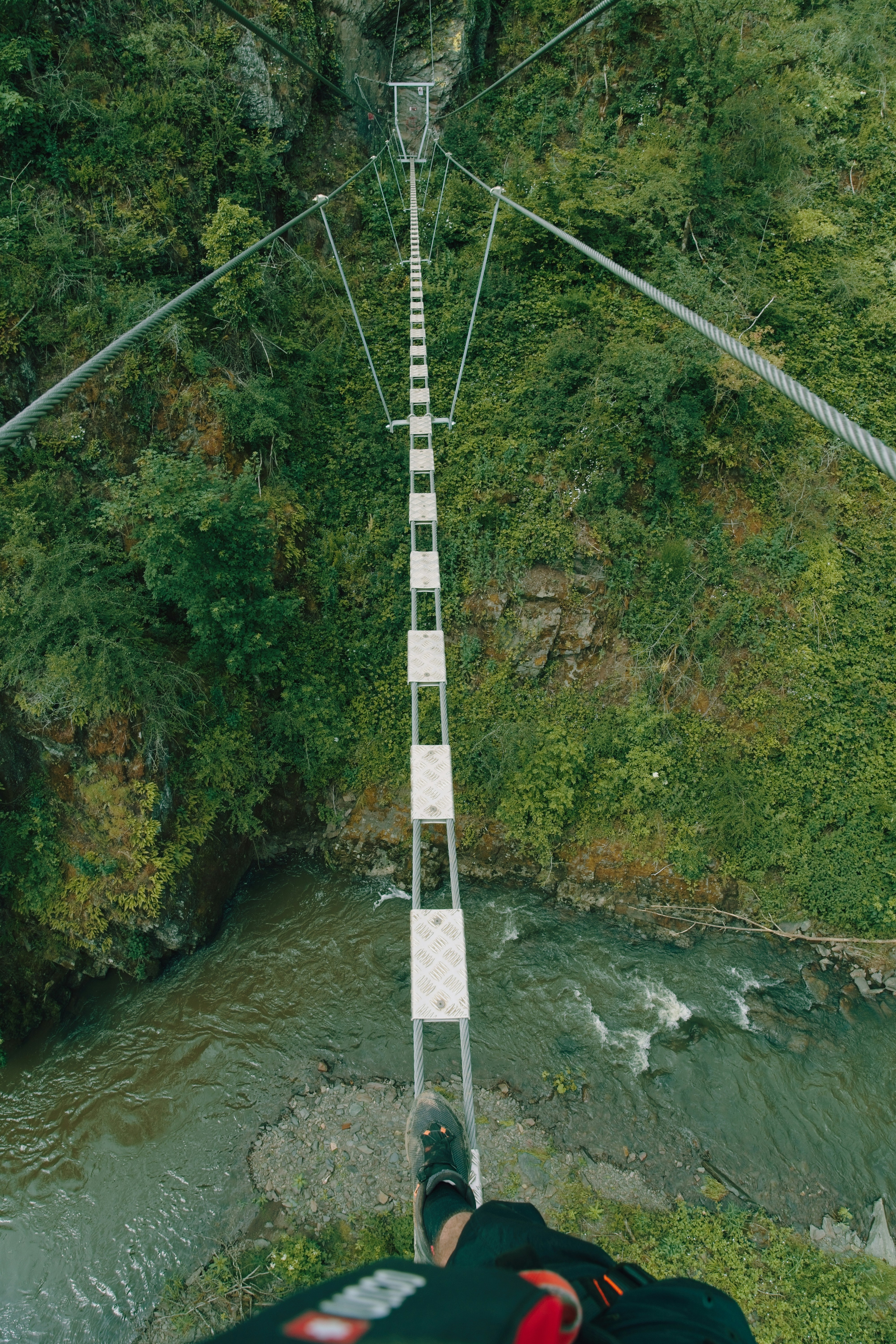 Person walking across a narrow suspension bridge over river.