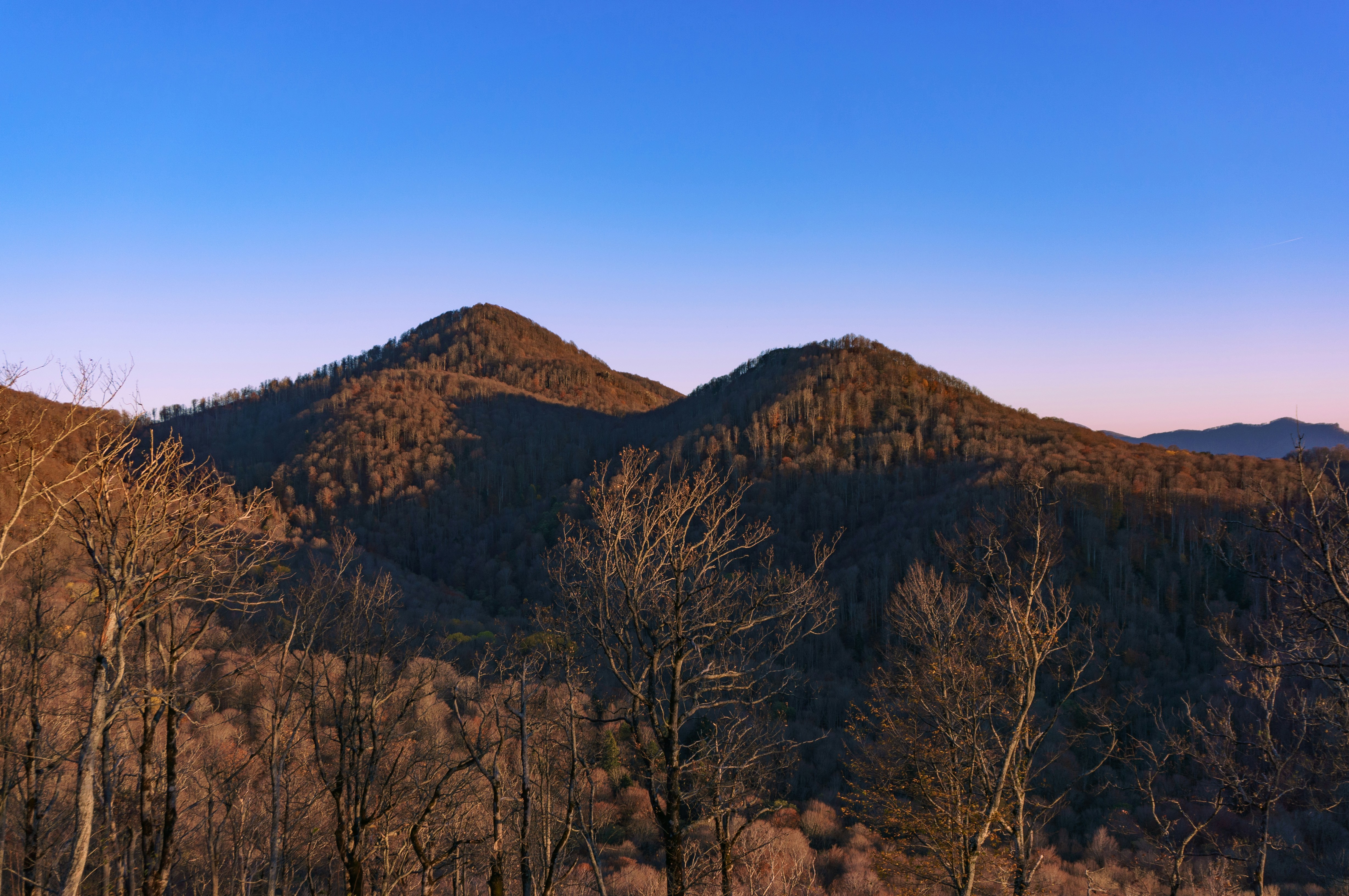Two tree-covered mountains under a clear blue sky