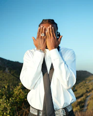 Man in white shirt covers face with hands outdoors background