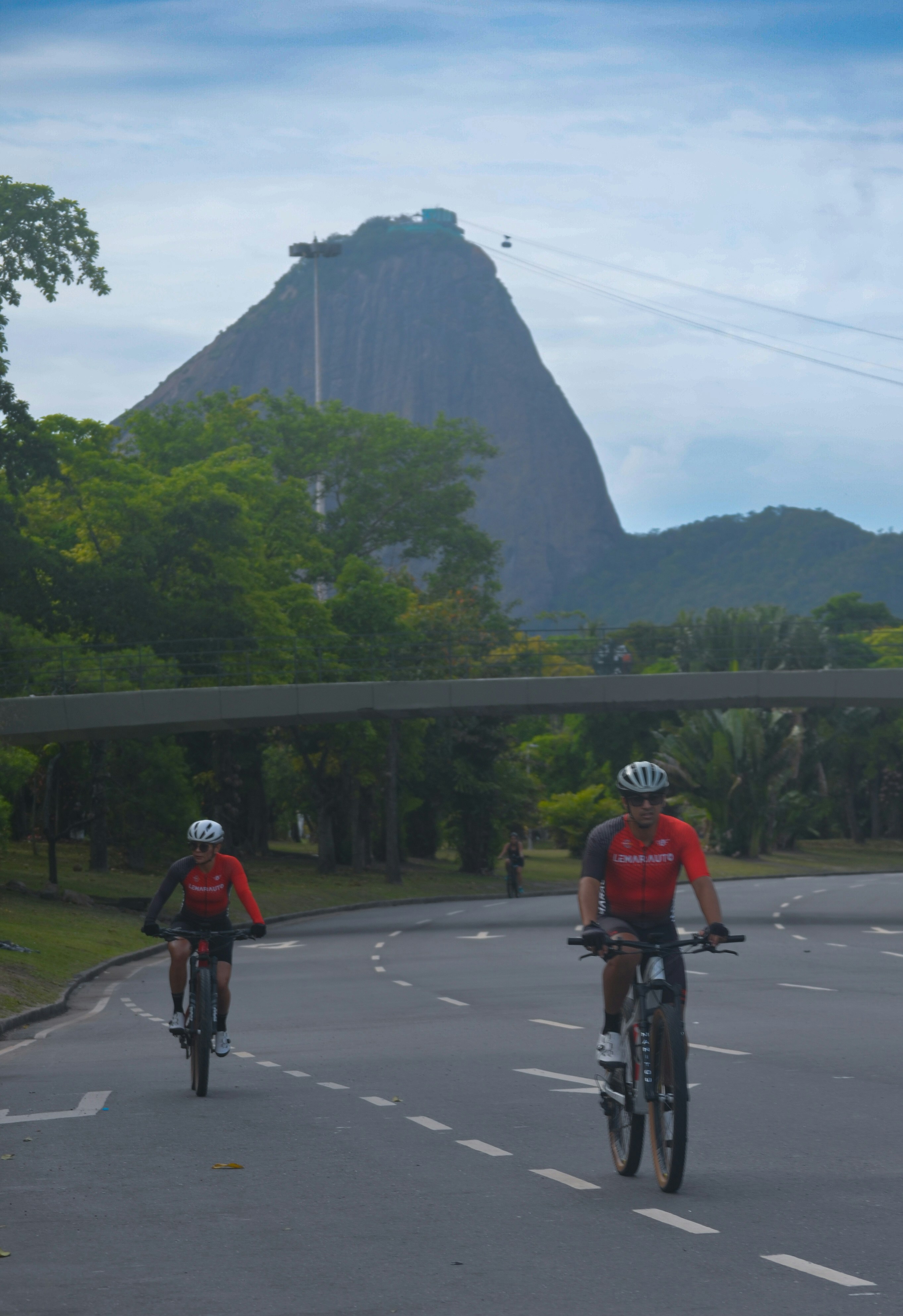 Two cyclists ride on a road with a mountain background