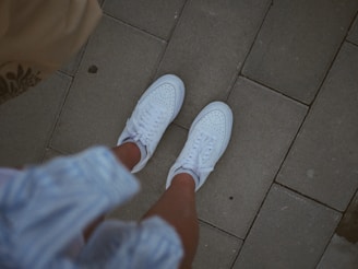 White sneakers on a person's feet walking on pavement.