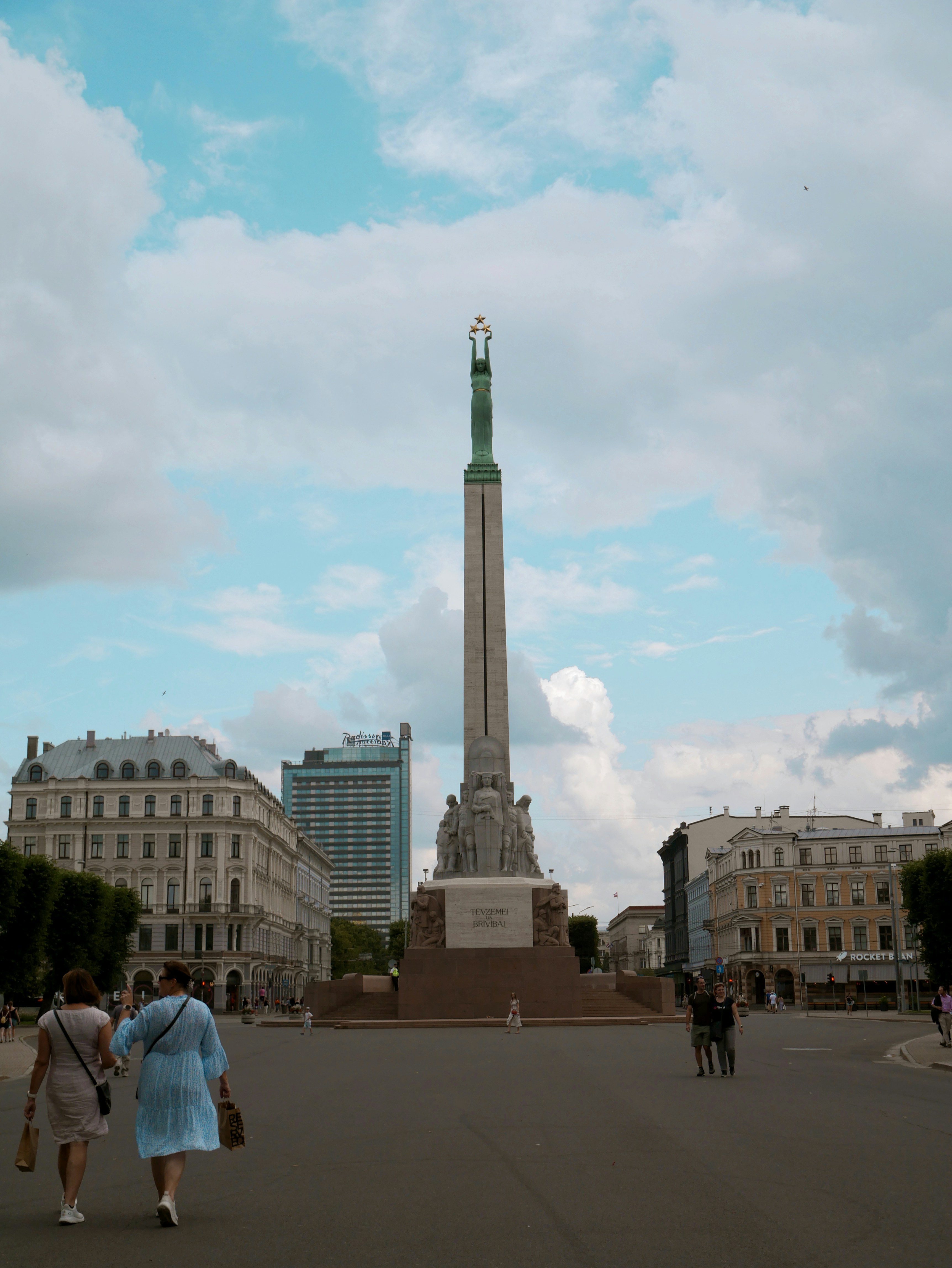Tall monument in a city square with people walking