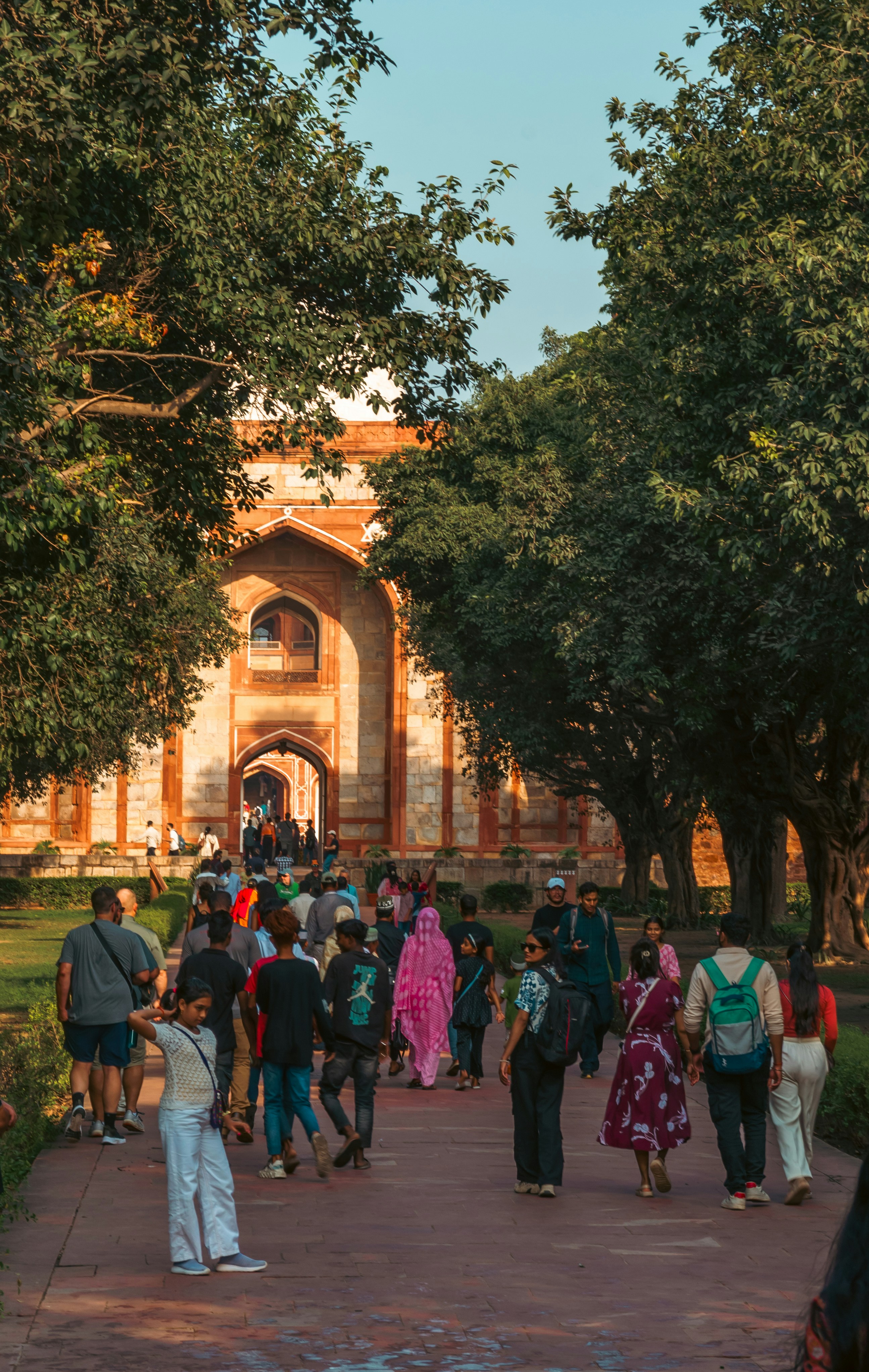 People walk towards a large arched building surrounded by trees.