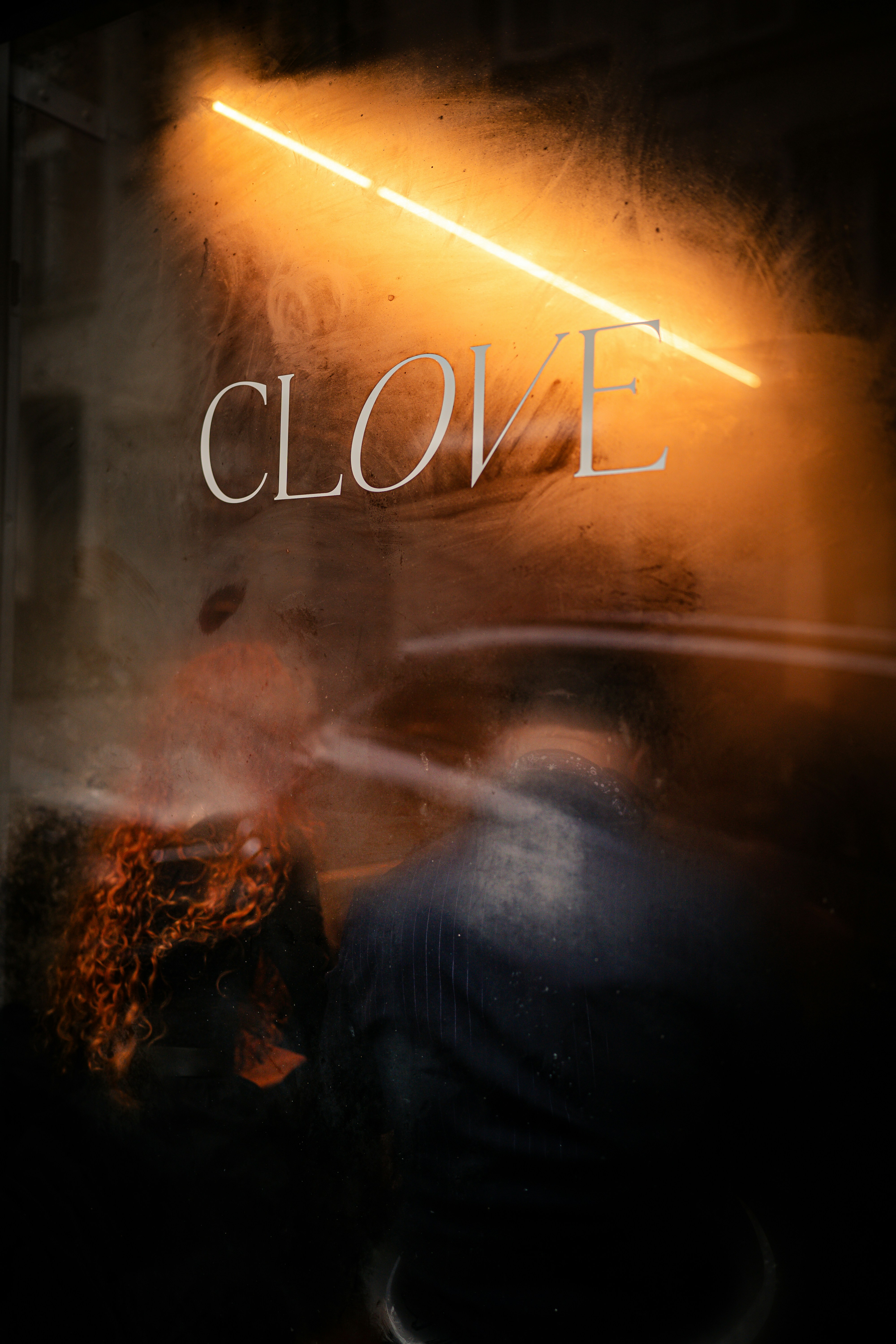 Neon sign above 'clove' on a foggy window.