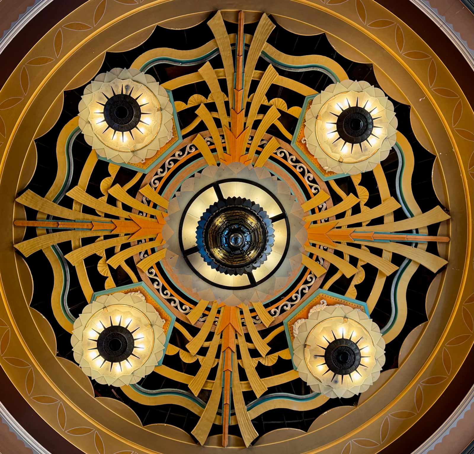 An Art Deco ceiling rosette in gold and black, lamps set in radiating rays.