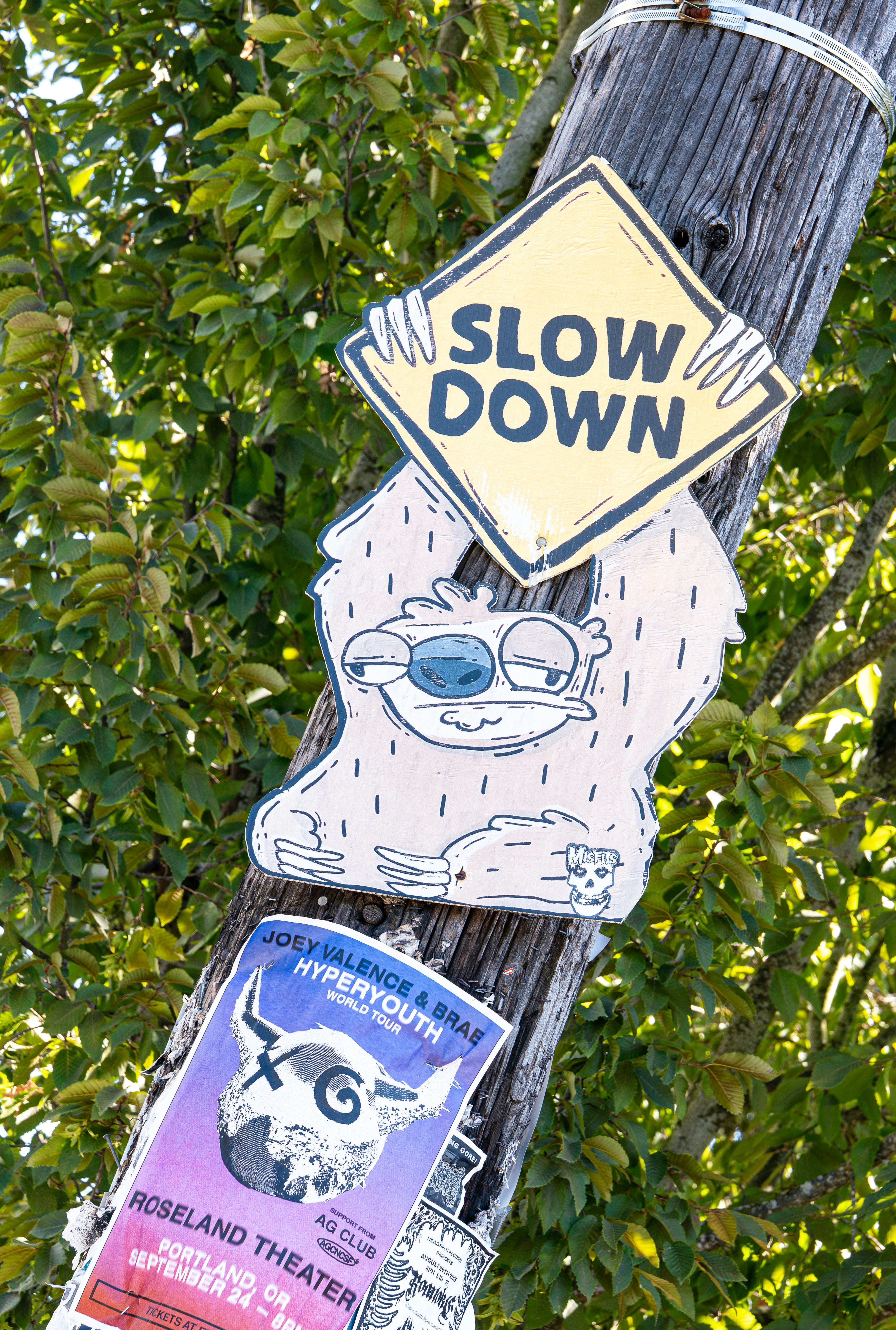 Wooden pole with 'slow down' sign and cartoon monster sticker.