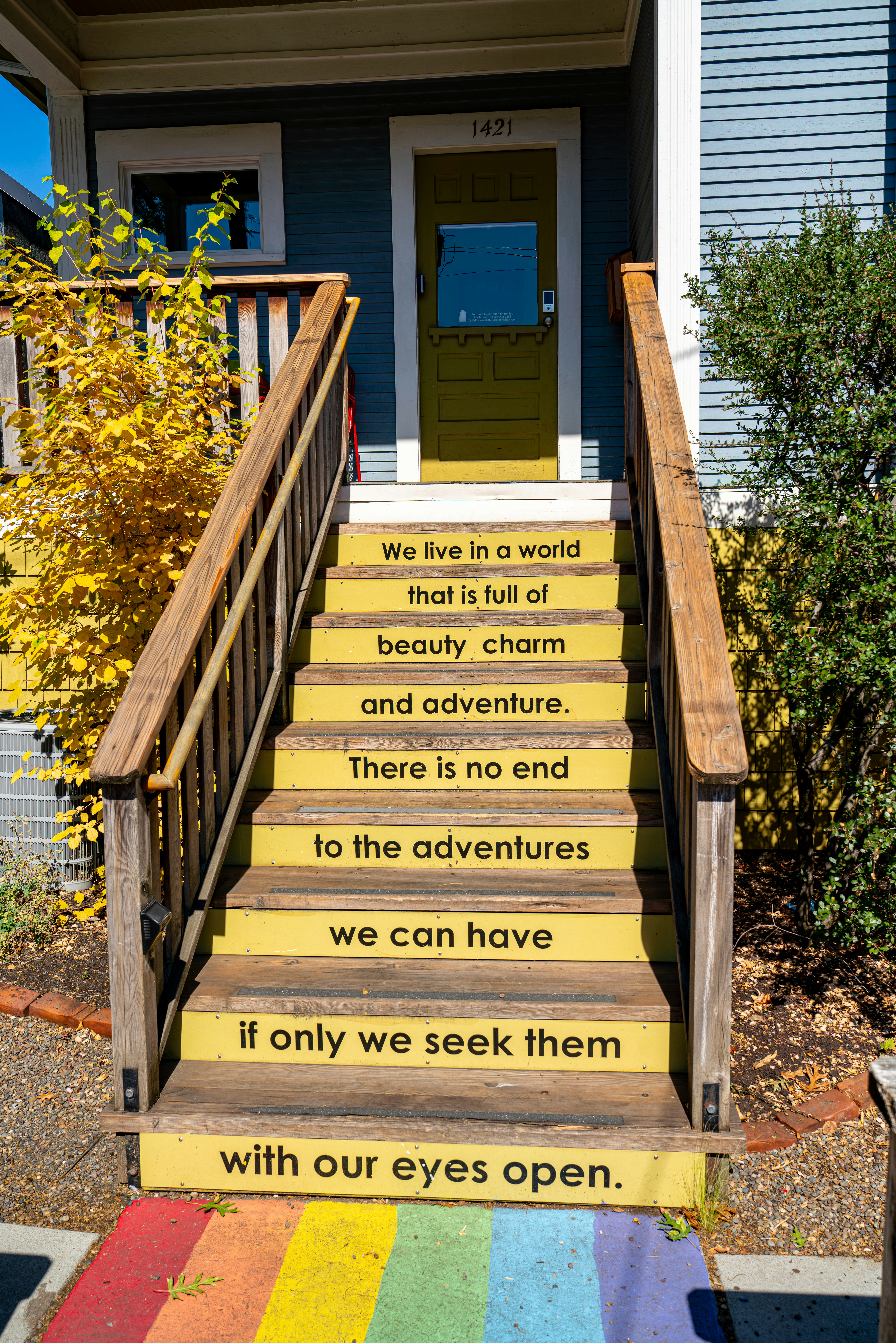 Escadas amarelas com citações inspiradoras e tapete arco-íris.