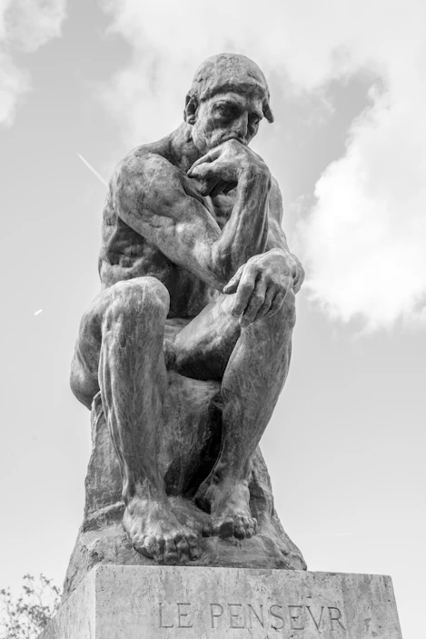 The thinker statue sits outdoors under a cloudy sky