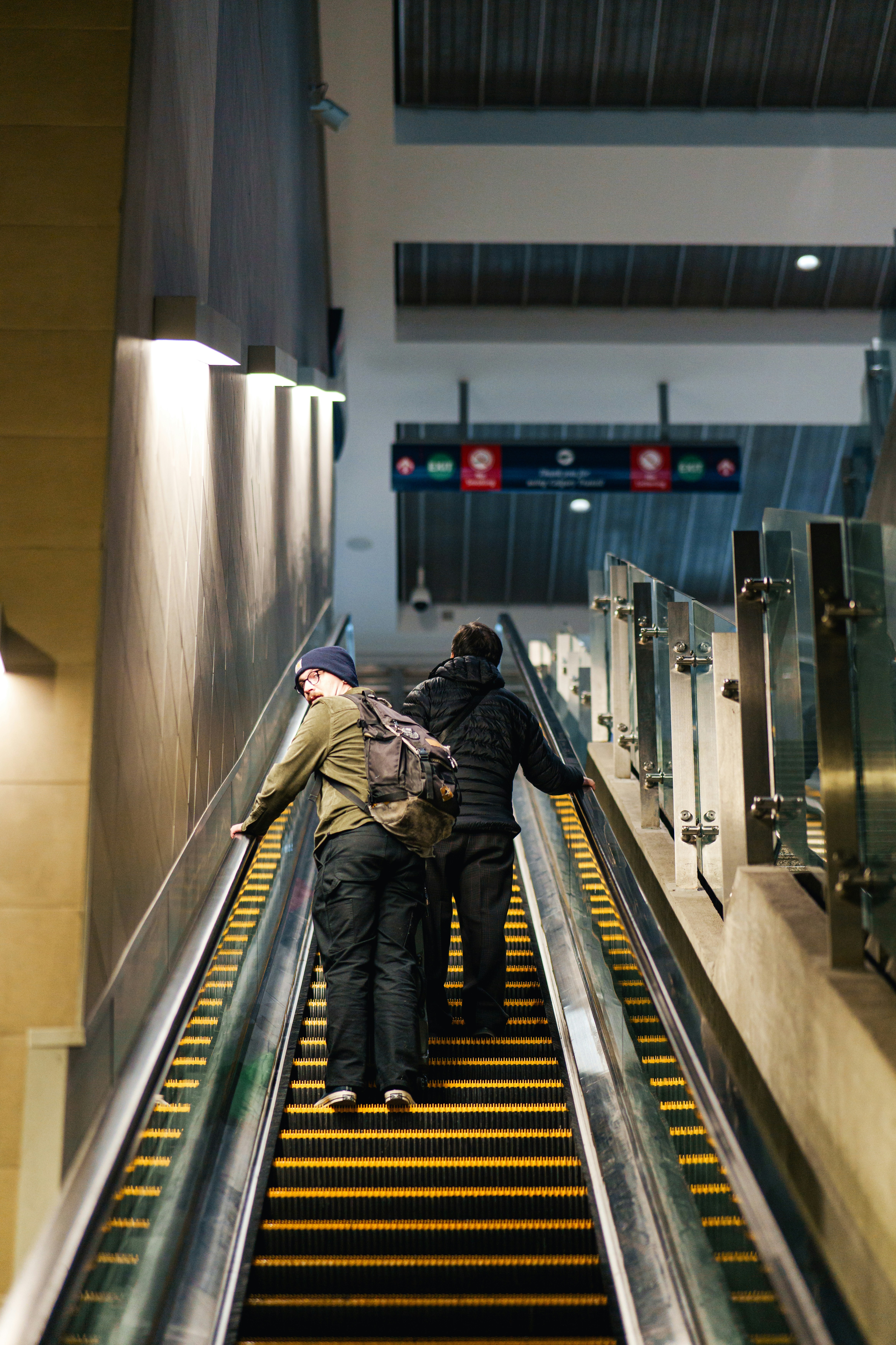 Zwei Personen steigen eine Rolltreppe in einem modernen Gebäude hinauf.