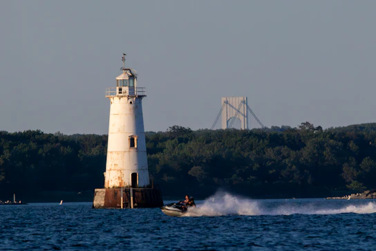 Jet ski speeds past lighthouse with bridge background