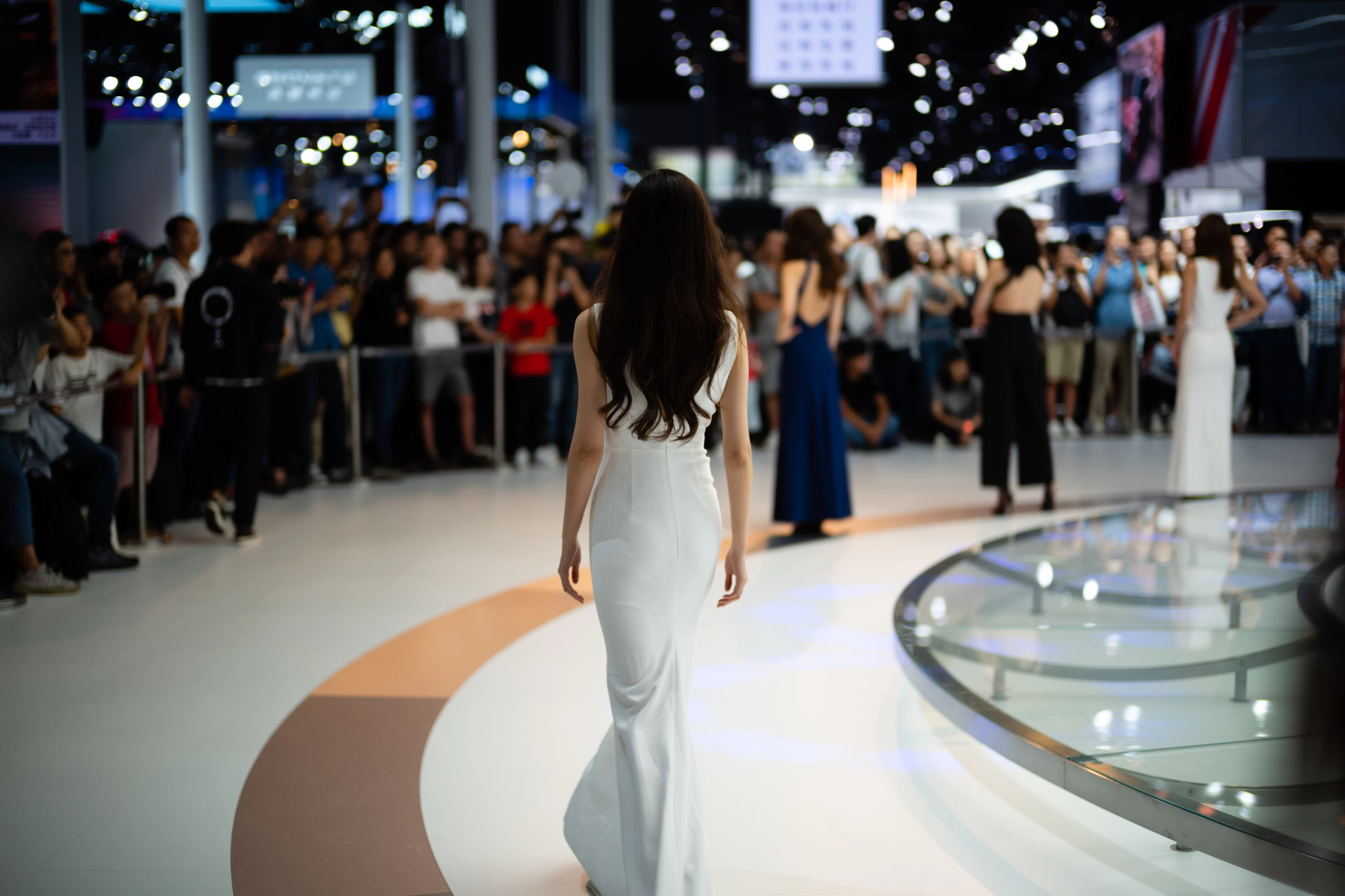 Model in a white gown walking a runway as a crowd watches
