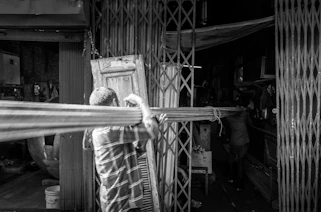 Man carrying long wooden beams through alleyway