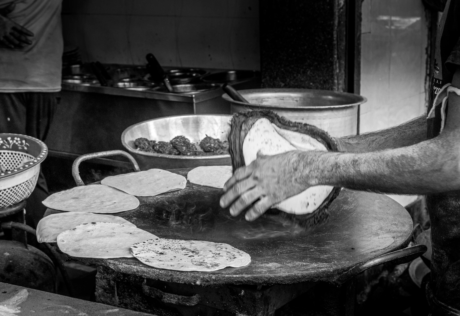 Hands preparing flatbread on a large griddle.