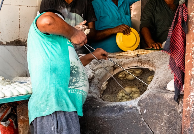 A baker shaping flatbread dough beside a hot clay tandir oven