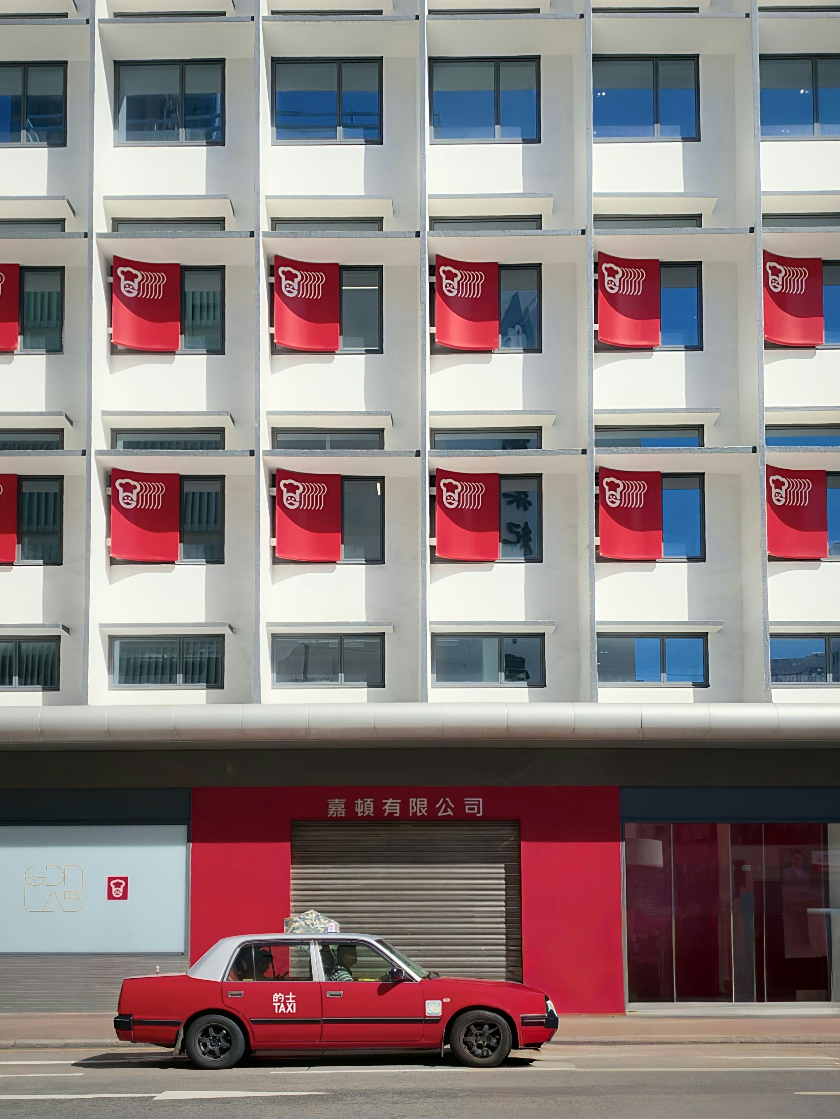 Red taxi parked in front of modern white building.